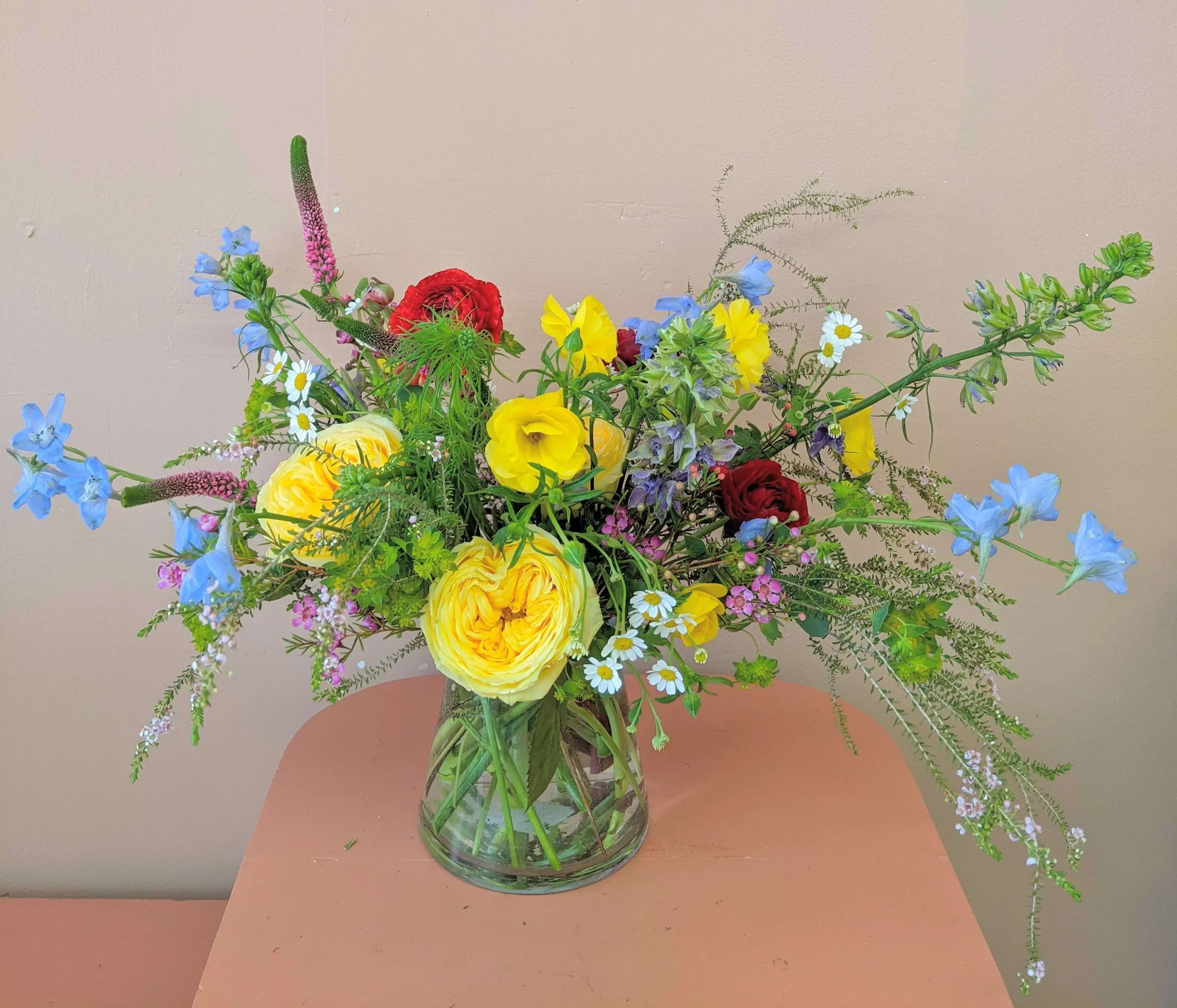 Mixed bouquet of yellow, red, and blue flowers in a clear glass vase