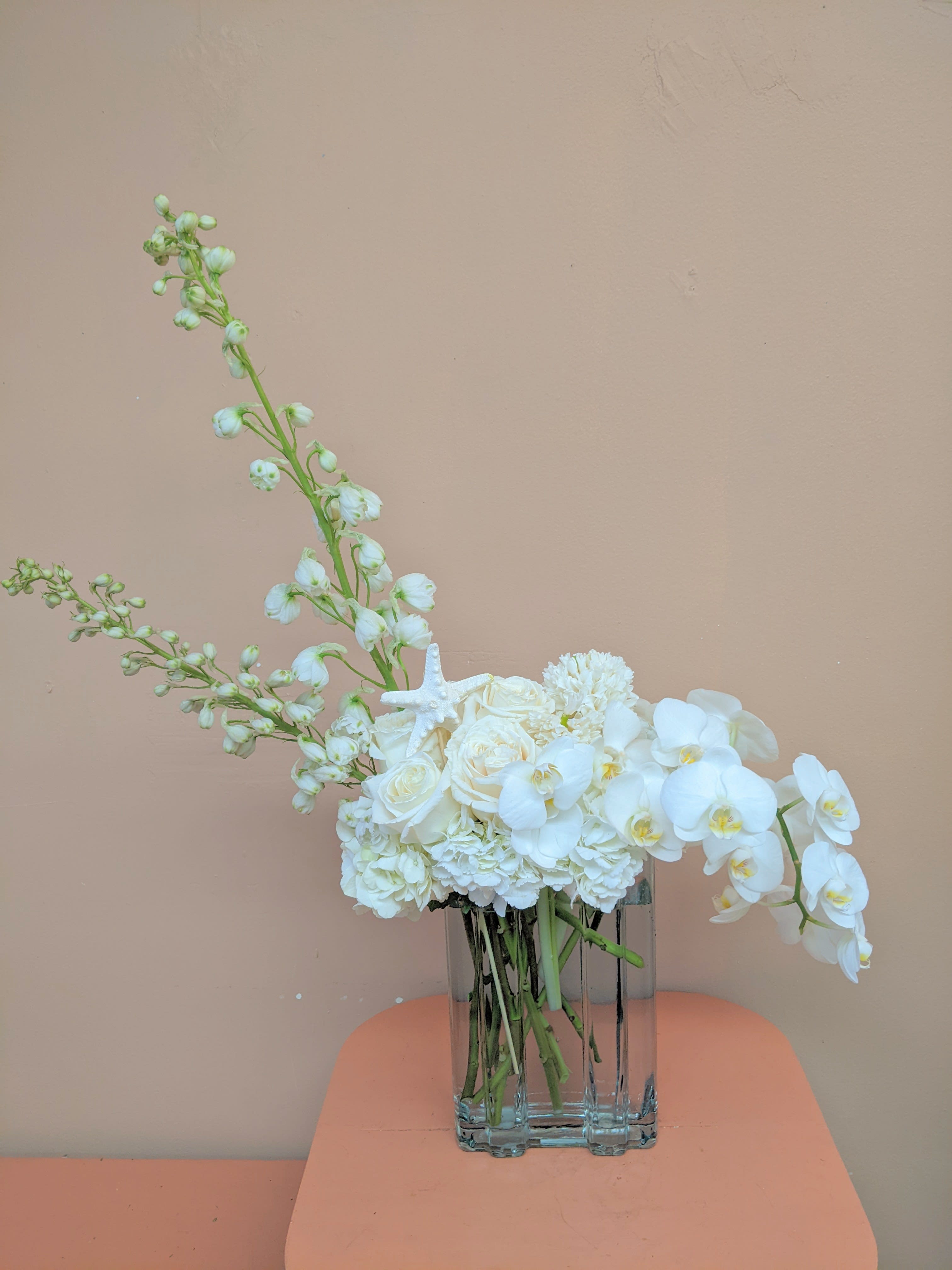 White floral arrangement in a clear glass vase with orchids and roses
