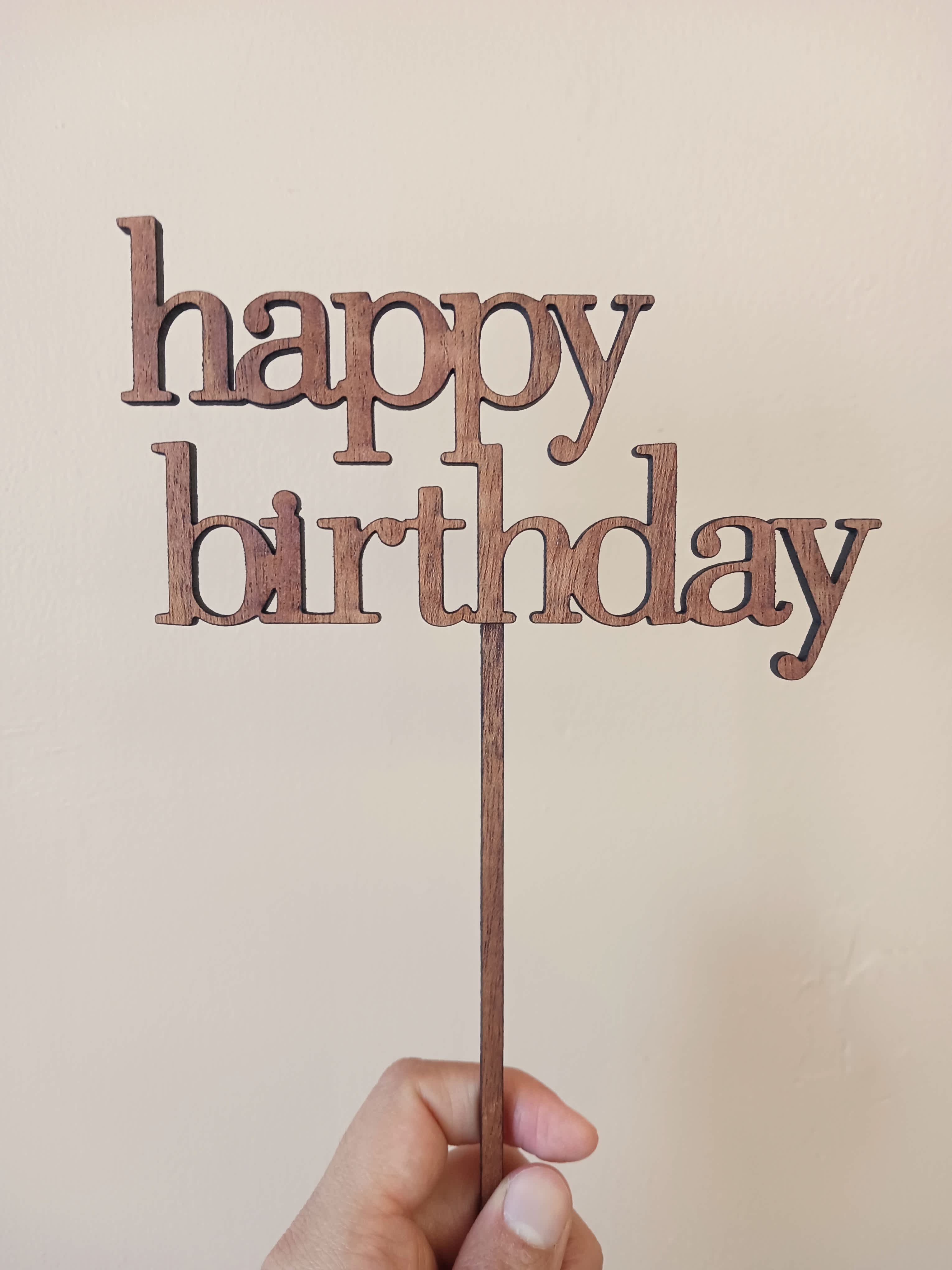 Wooden "happy birthday" cake topper held in a hand