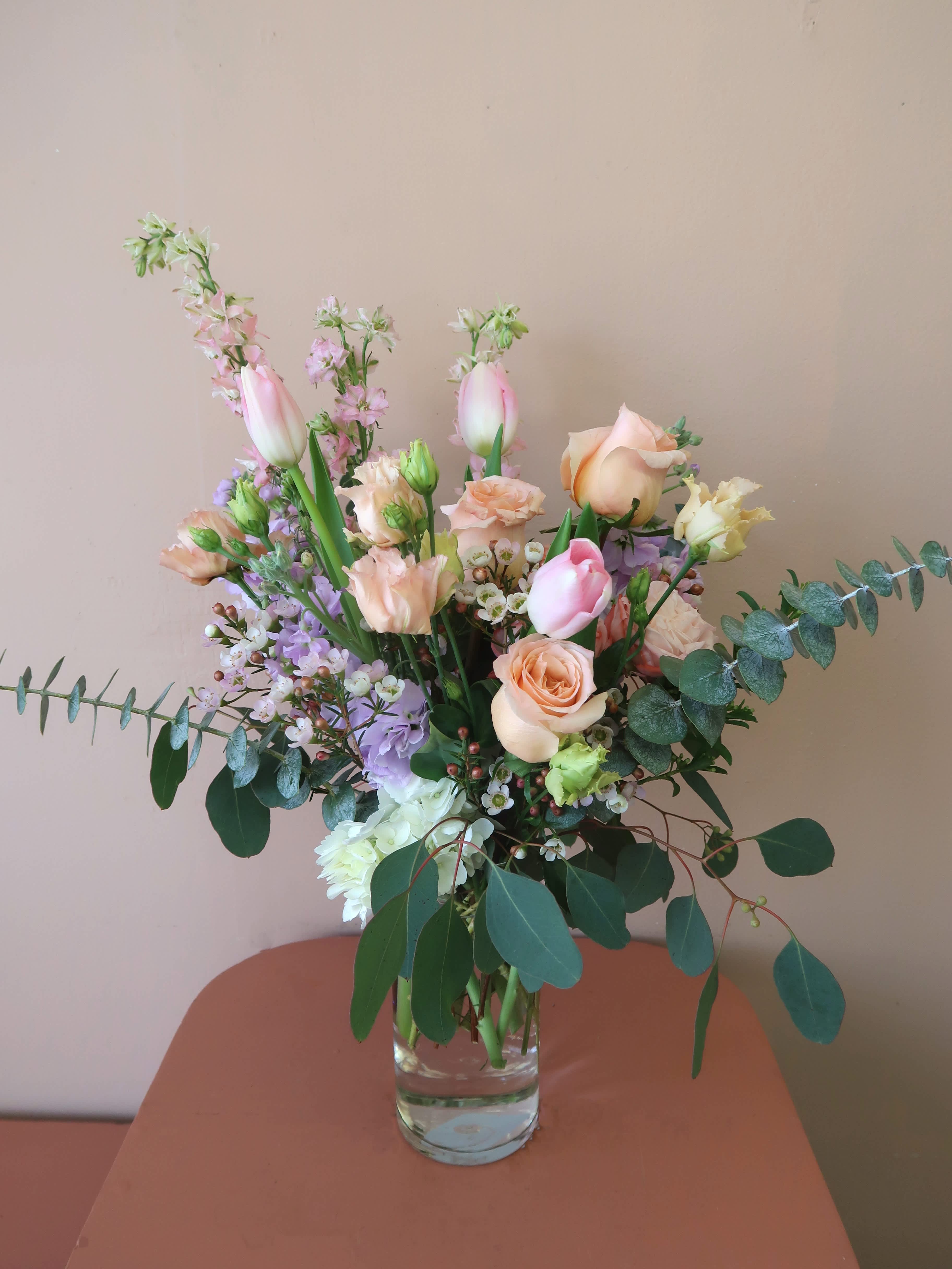Mixed pastel bouquet in a clear glass vase with roses and tulips