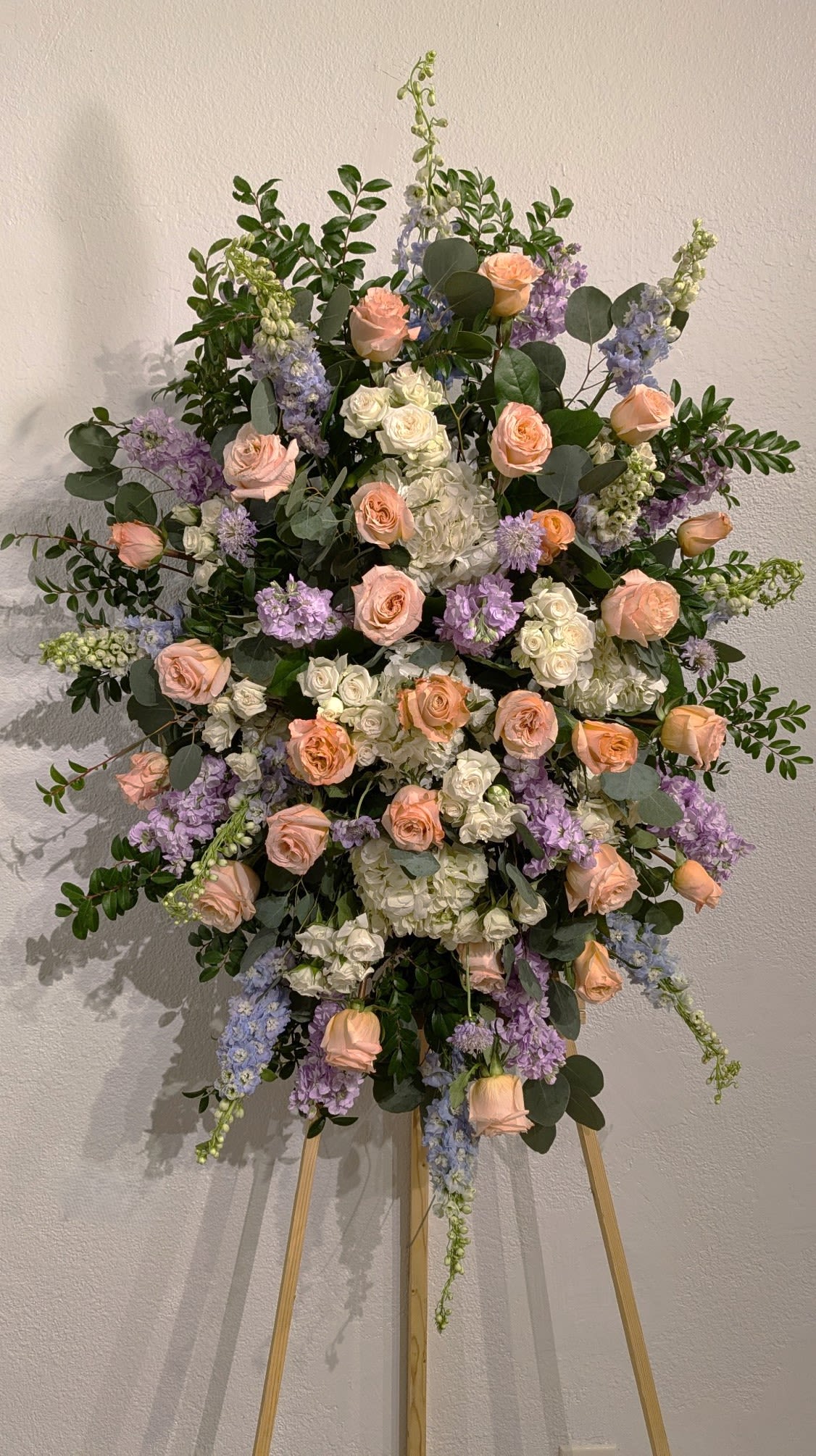 Large floral spray of peach roses, white blooms, and lavender flowers on an easel