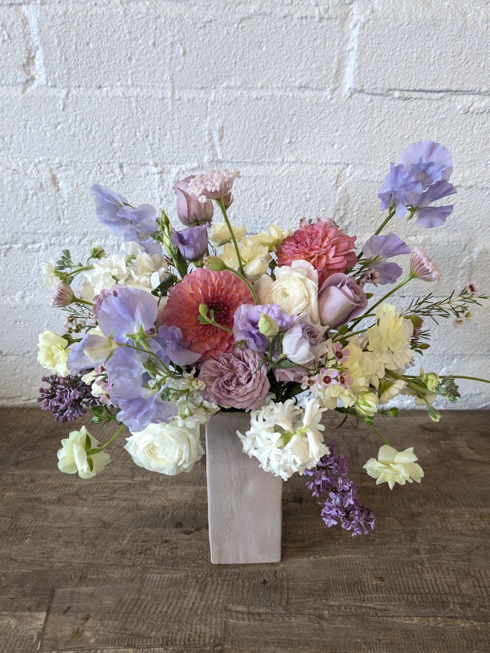 Lavender Grace - A subtle assortment of lavenders with a pop of peach in a matte, clay vase. 