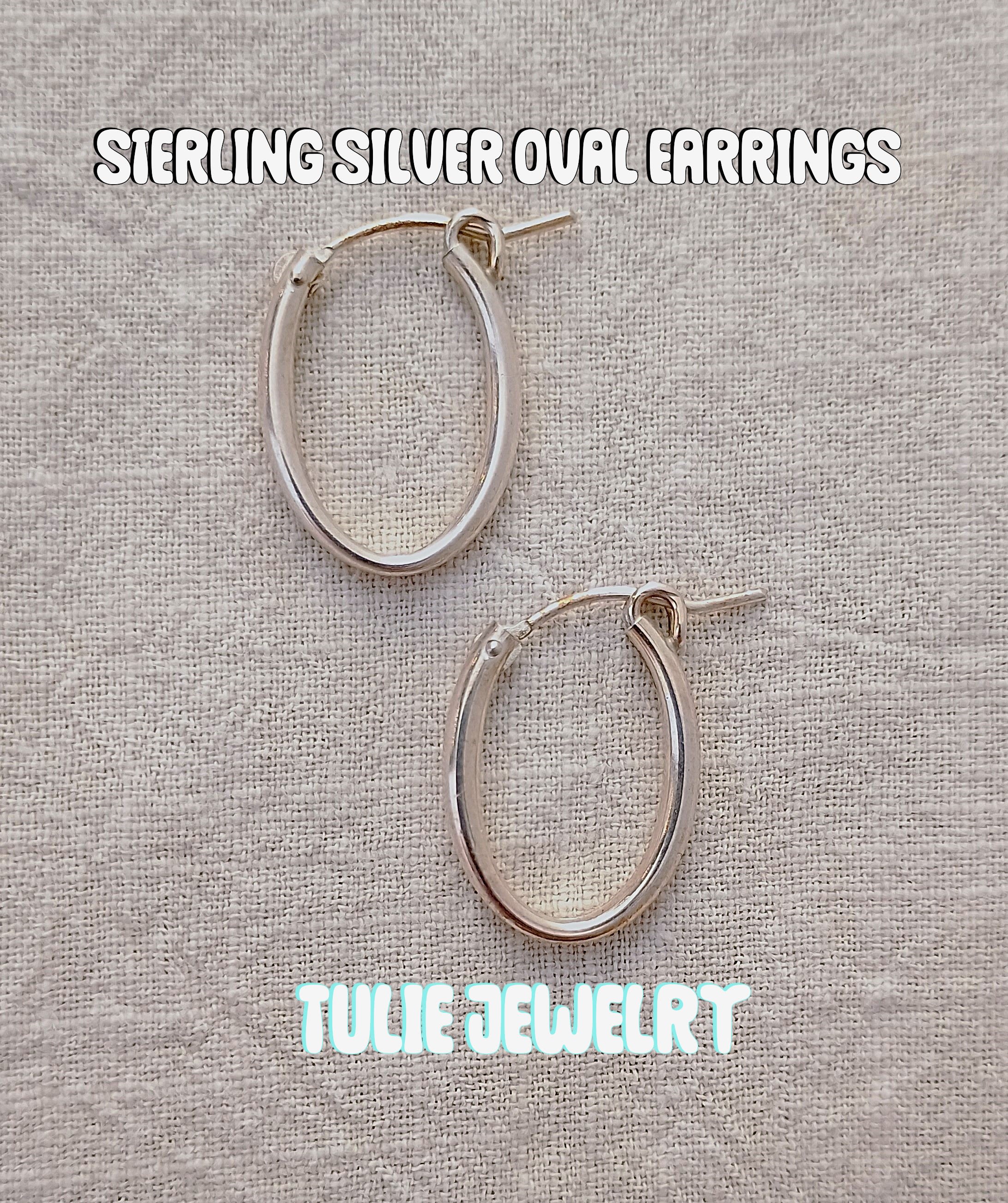 Pair of silver oval hoop earrings on a textured fabric background