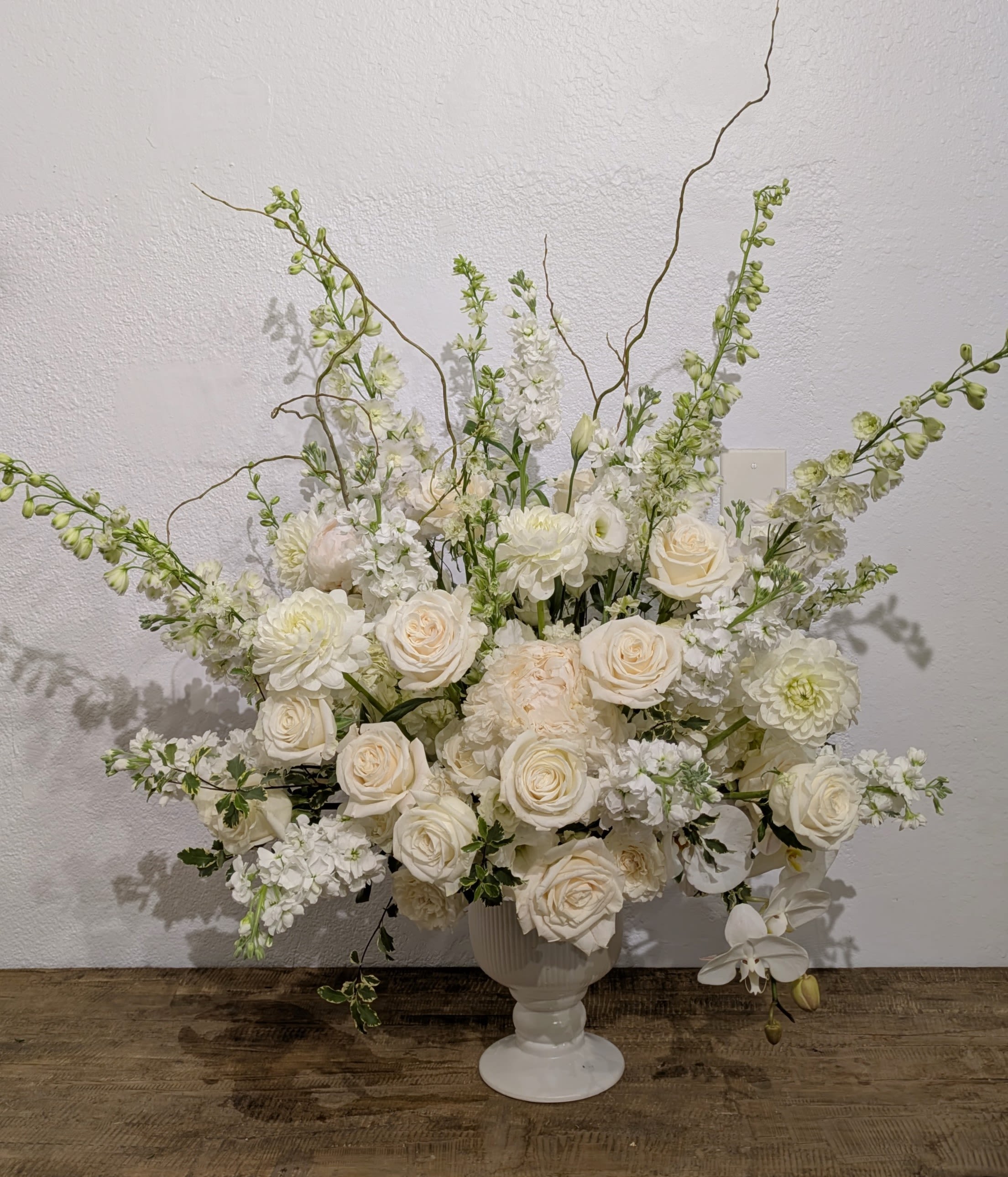 White floral arrangement in a white pedestal vase with tall branching stems
