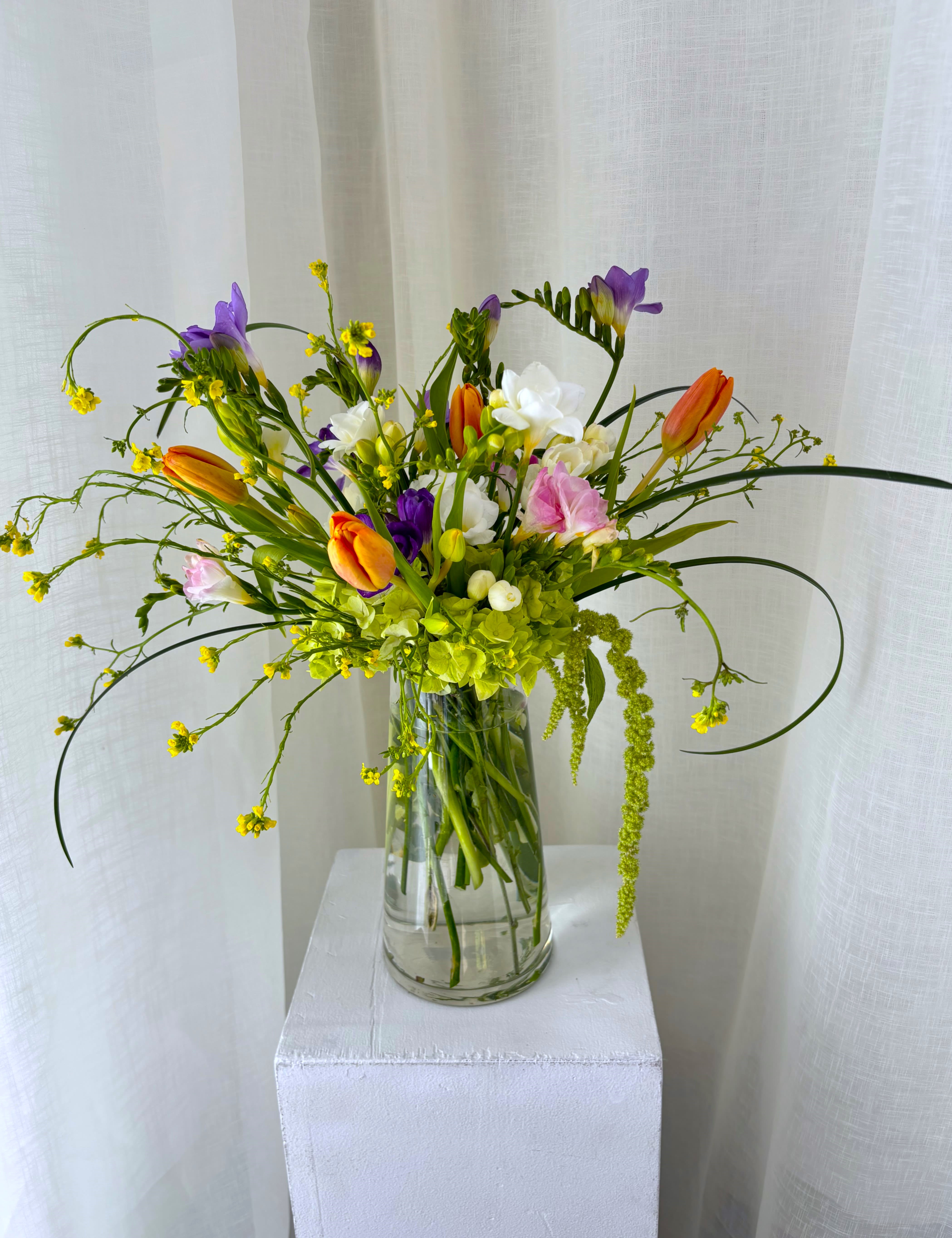 Mixed bouquet of orange tulips, purple freesia, and white blooms in a glass vase