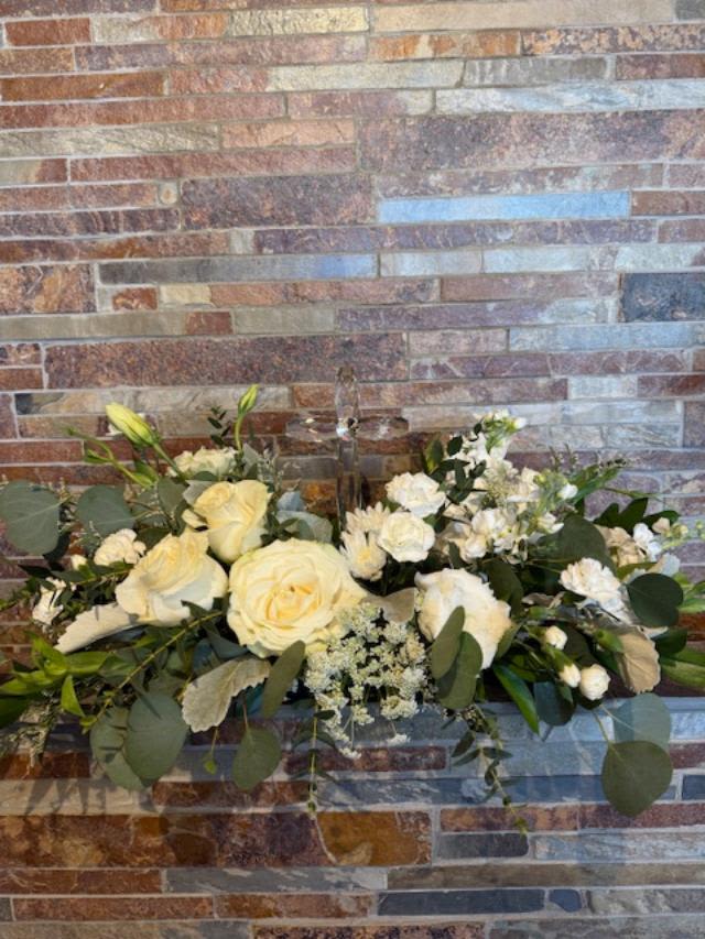 White rose arrangement with greenery against a brick wall