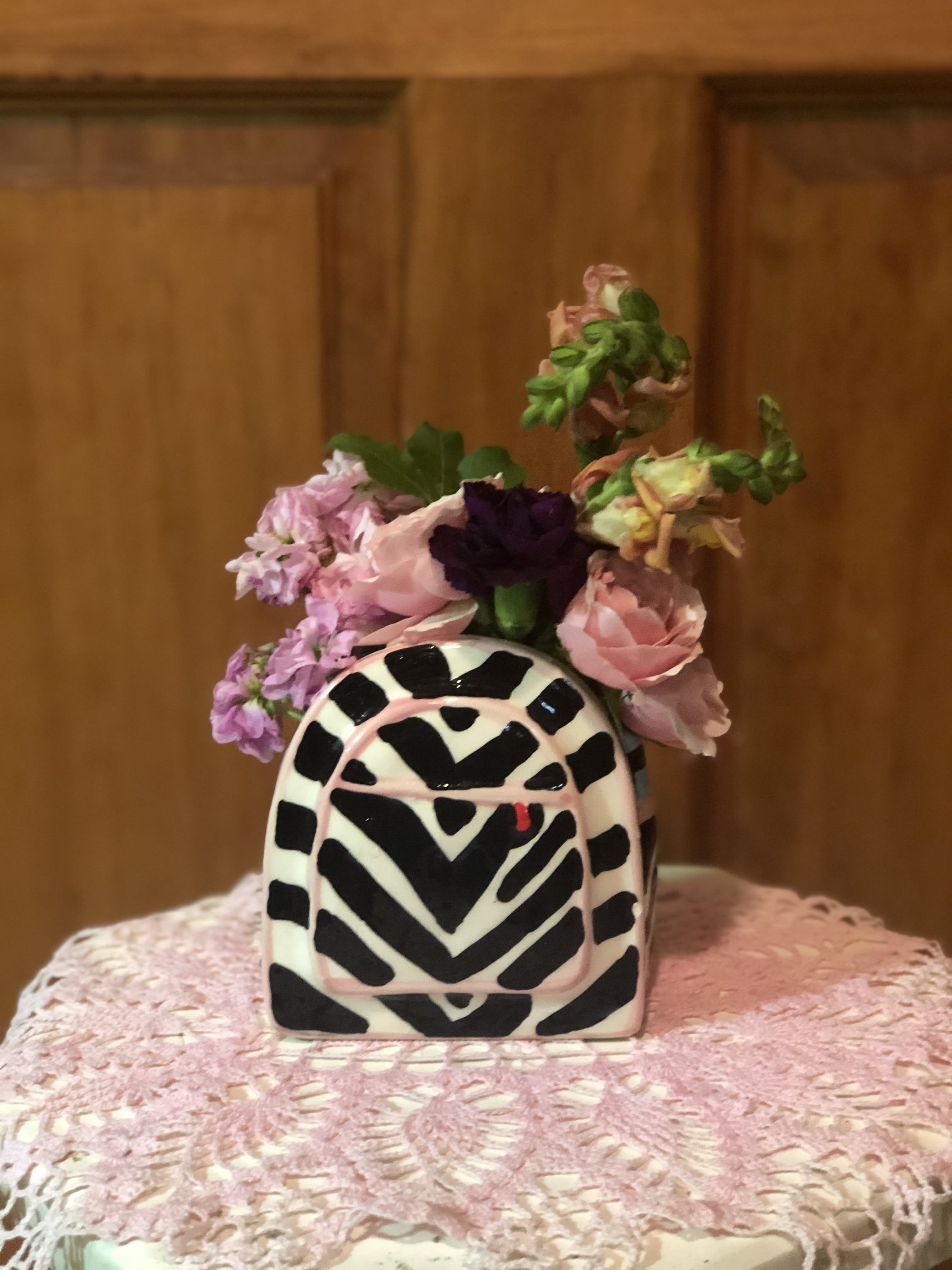 Small pink and purple flower arrangement in a black-and-white patterned vase