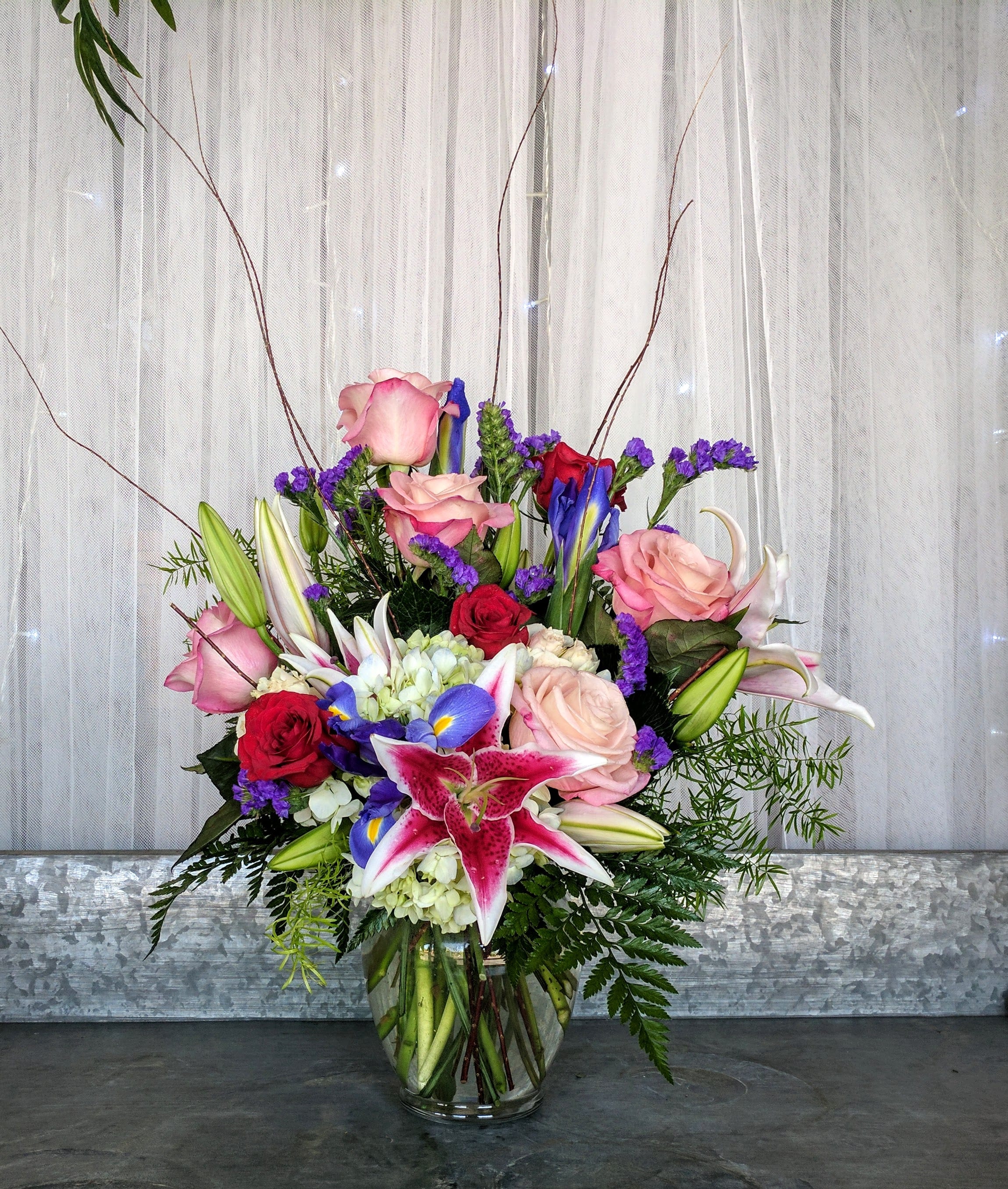 Star - Filled with red Roses, bi-color pink Roses, blue Iris, purple Statice, white Hydrangea and Stargazer Lilies surrounded by beautiful foliage and accented with Curly Willow or similar greens and flowers.  This is a stunning arrangement that will definitely send a message.