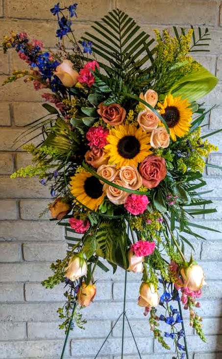 Summer Memories - A bright and cheerful summer easel stand filled with colorful Roses, Sunflowers, Snapdragons, blue Delphinium, pink Carnation, Salidago or similar flowers and accented with beautiful foliage. A great way to brighten up a gathering or to send your message of love to a lost loved one.