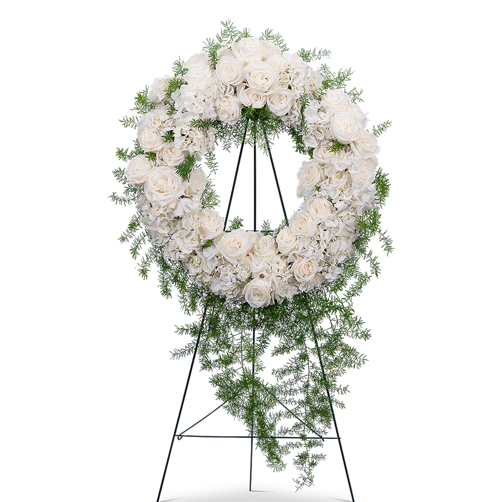 Eternal Peace Wreath - Whether sent from family, co-workers, or friends, a standing spray or wreath is an appropriate gift of condolence. Our Eternal Peace Wreath features white roses, hydrangea, stock, springeri, and premium foliage. All white sympathy arrangements are classic and beautiful, allowing you to demonstrate the purity of your love and respect for your lost loved one or friend. The circular shape of a wreath in a funeral symbolizes eternal life and is a beautiful way to send your sympathy.   The image shows the Deluxe arrangement.