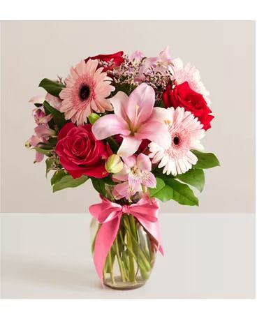 Bouquet of pink and red flowers in a glass vase with a pink ribbon