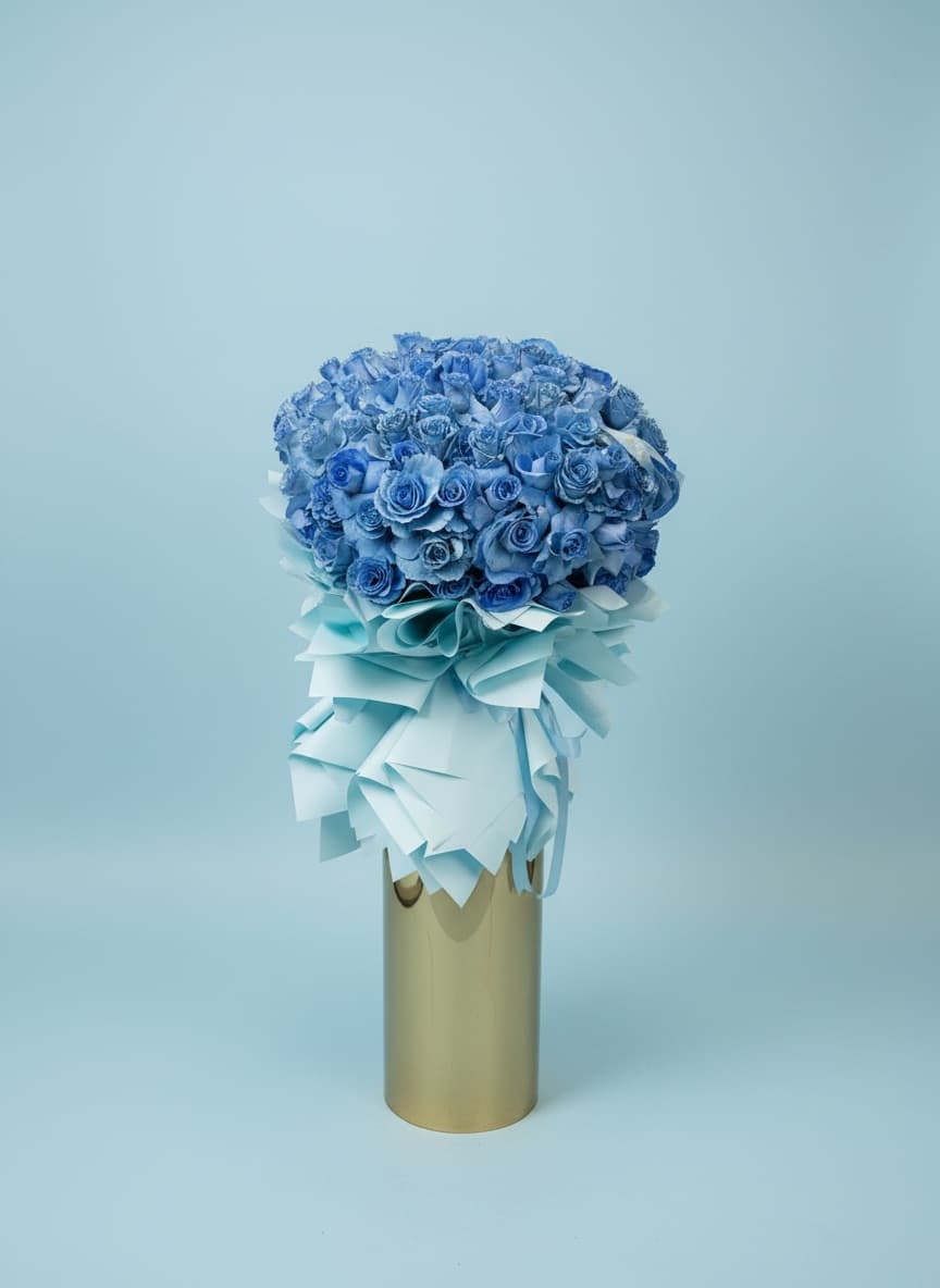 Blue rose bouquet with a pale ribbon wrap in a gold vase
