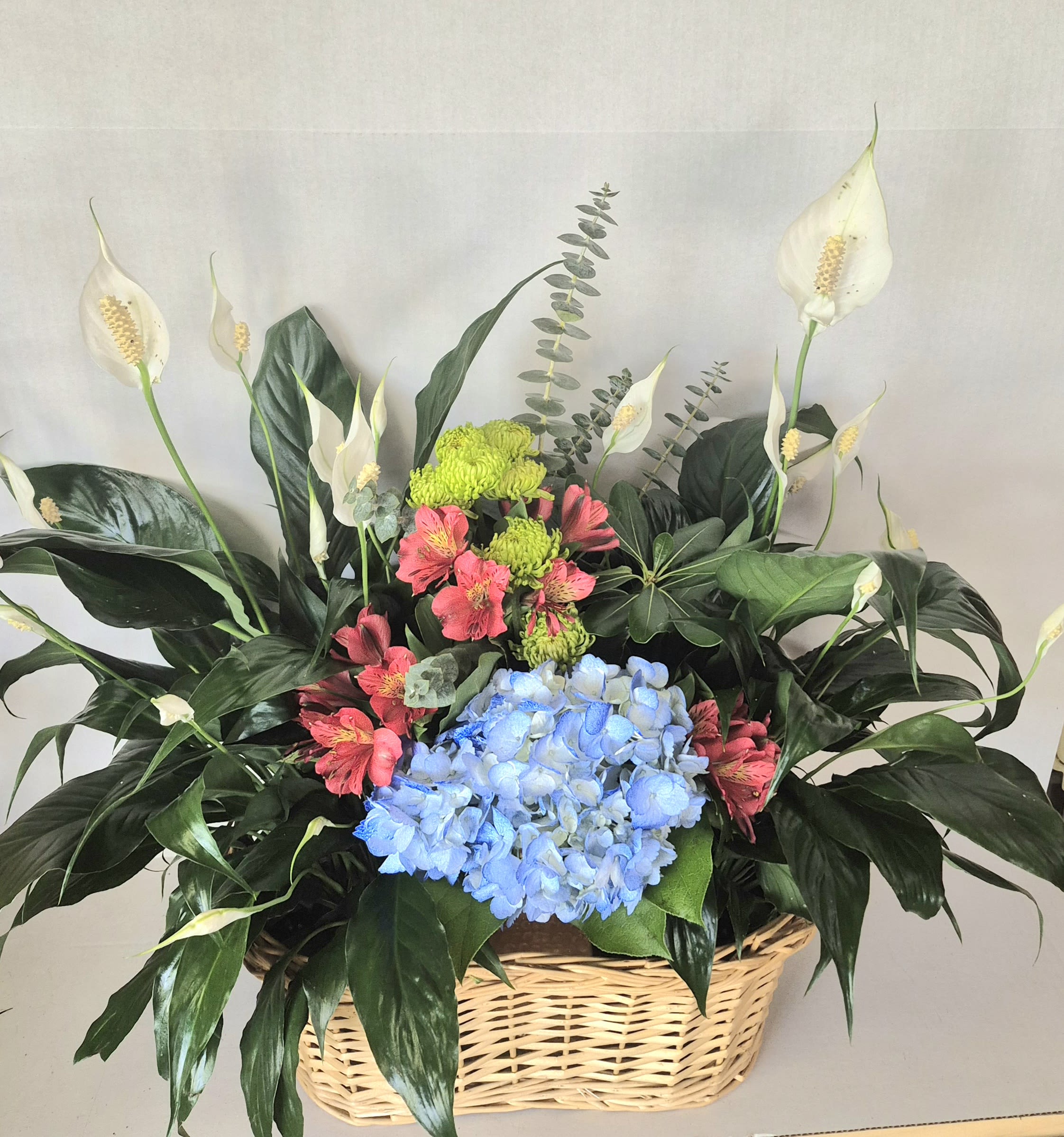 Basket arrangement with blue hydrangeas, pink alstroemeria, and white peace lilies