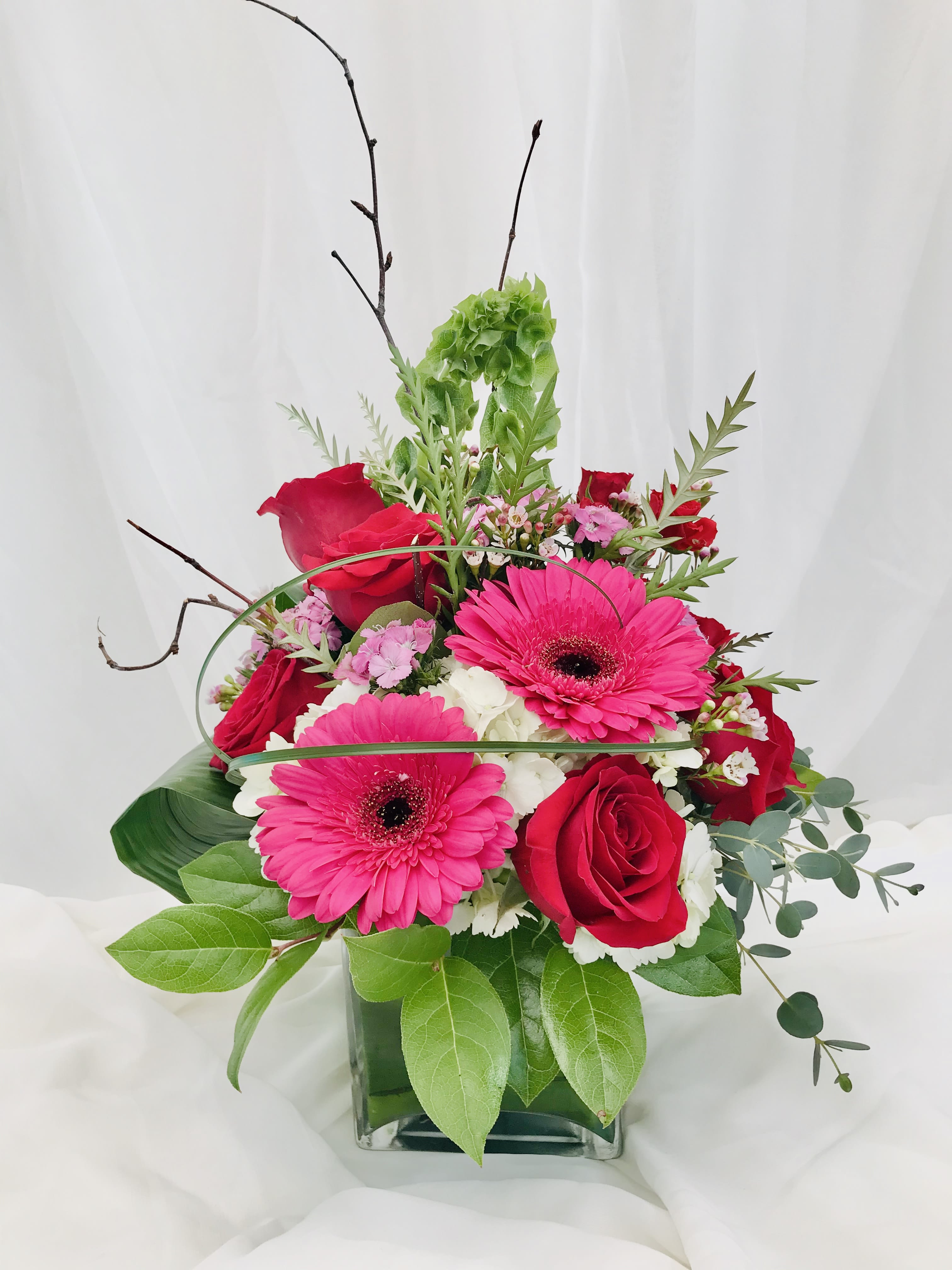 Pink gerbera daisies and red roses arranged in a glass vase
