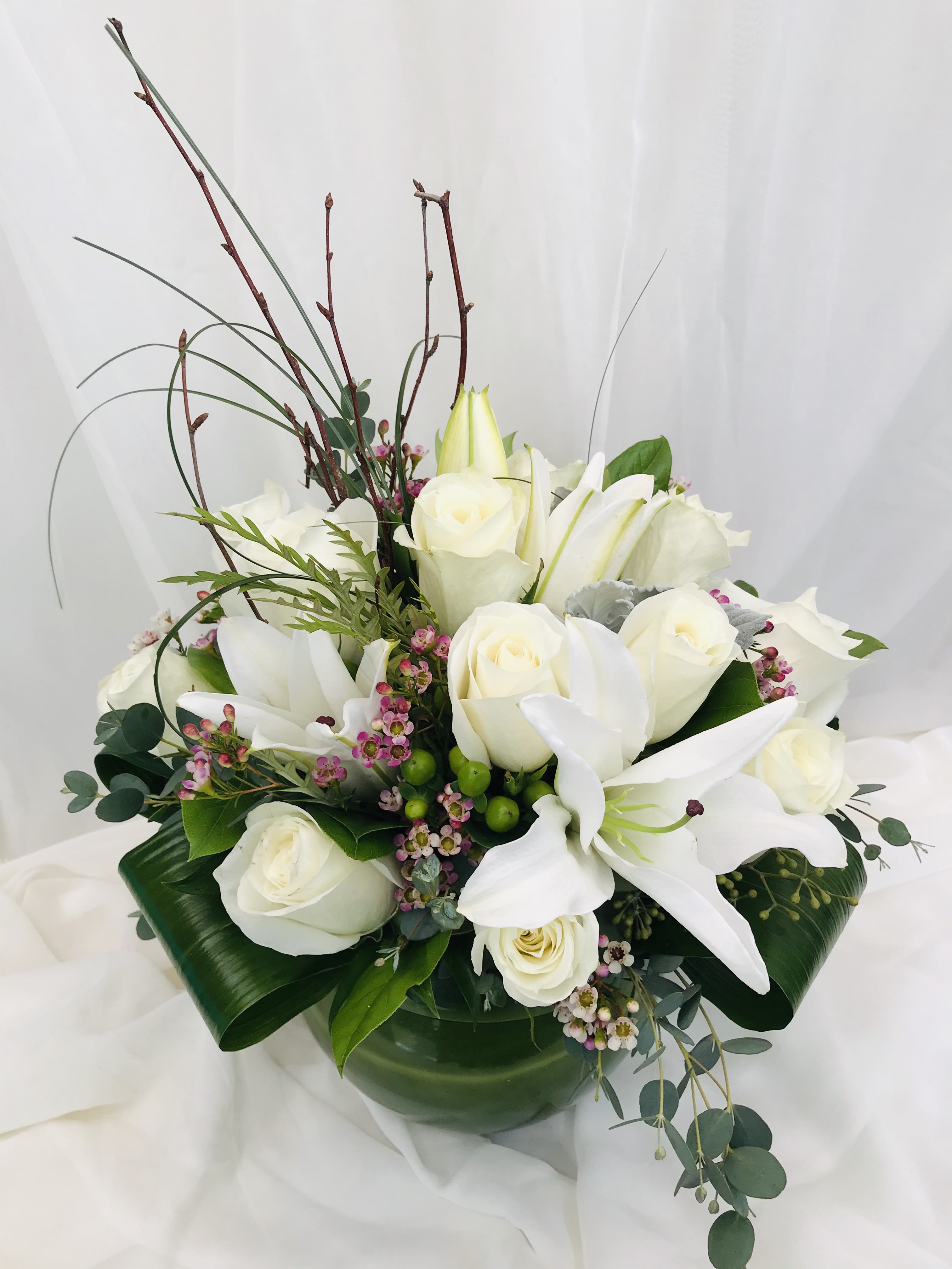 White roses and lilies arranged in a low vase with greenery