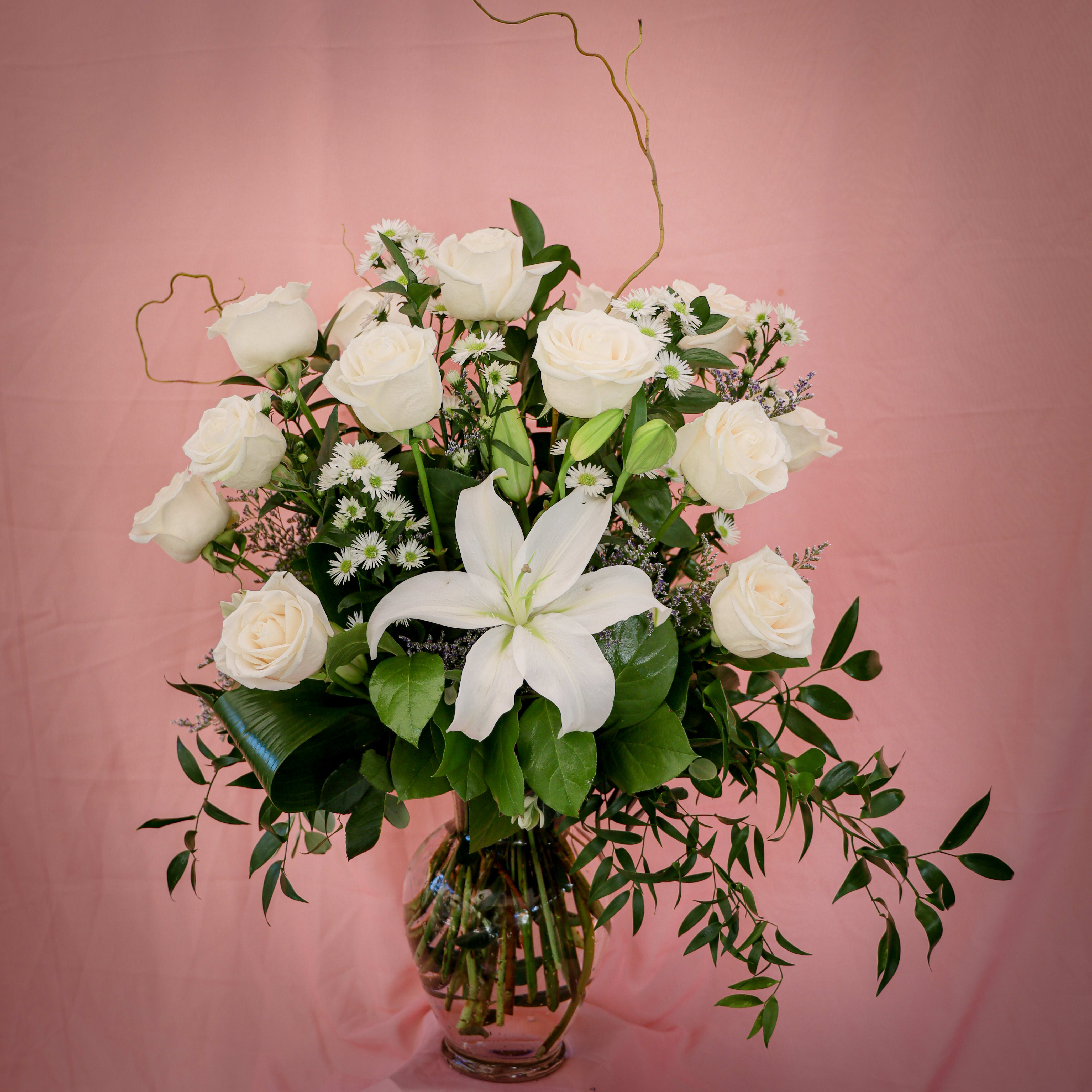 White roses and a white lily in a glass vase with small daisy flowers