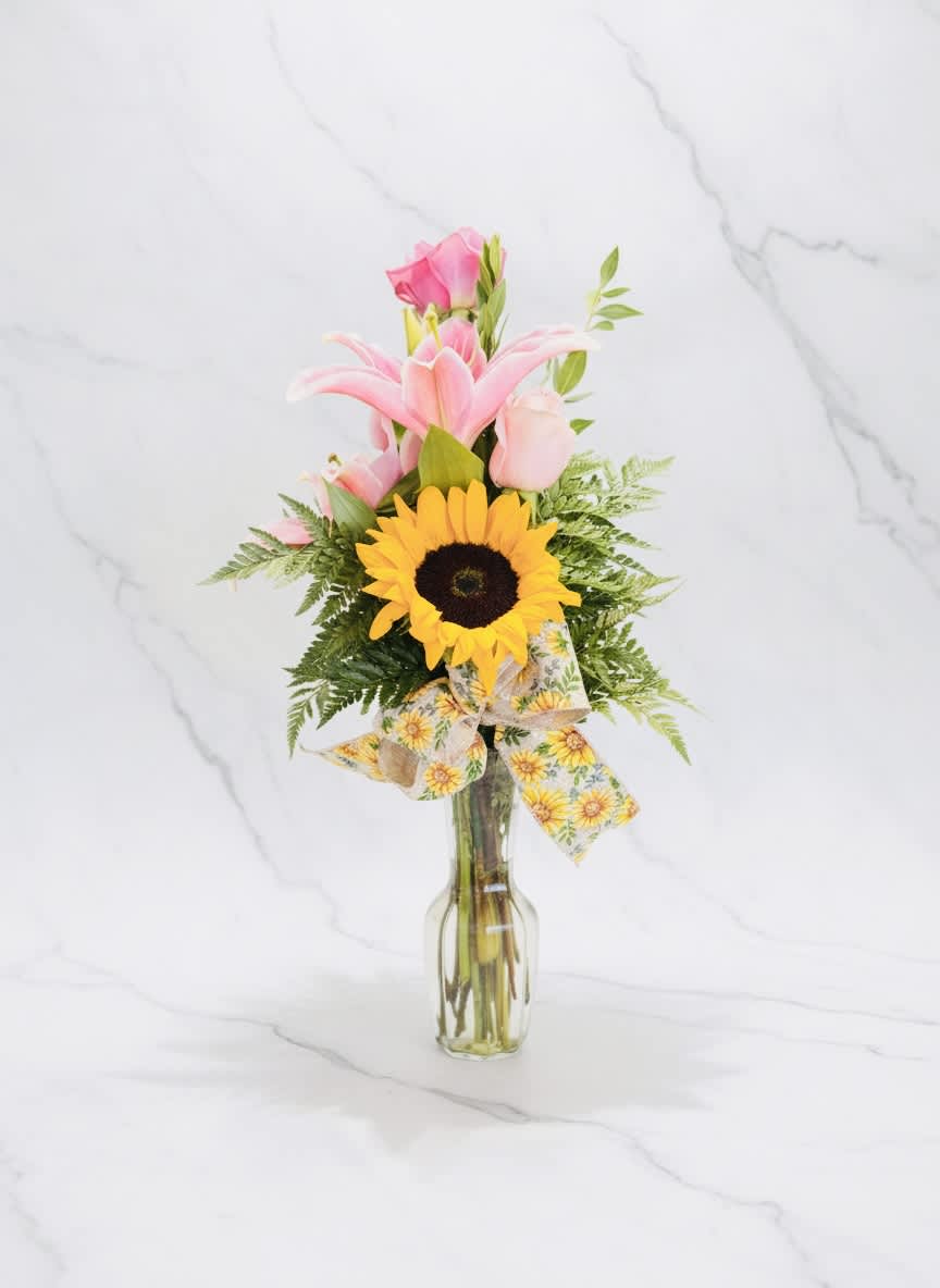 Pink lilies and a sunflower in a clear glass vase with a ribbon