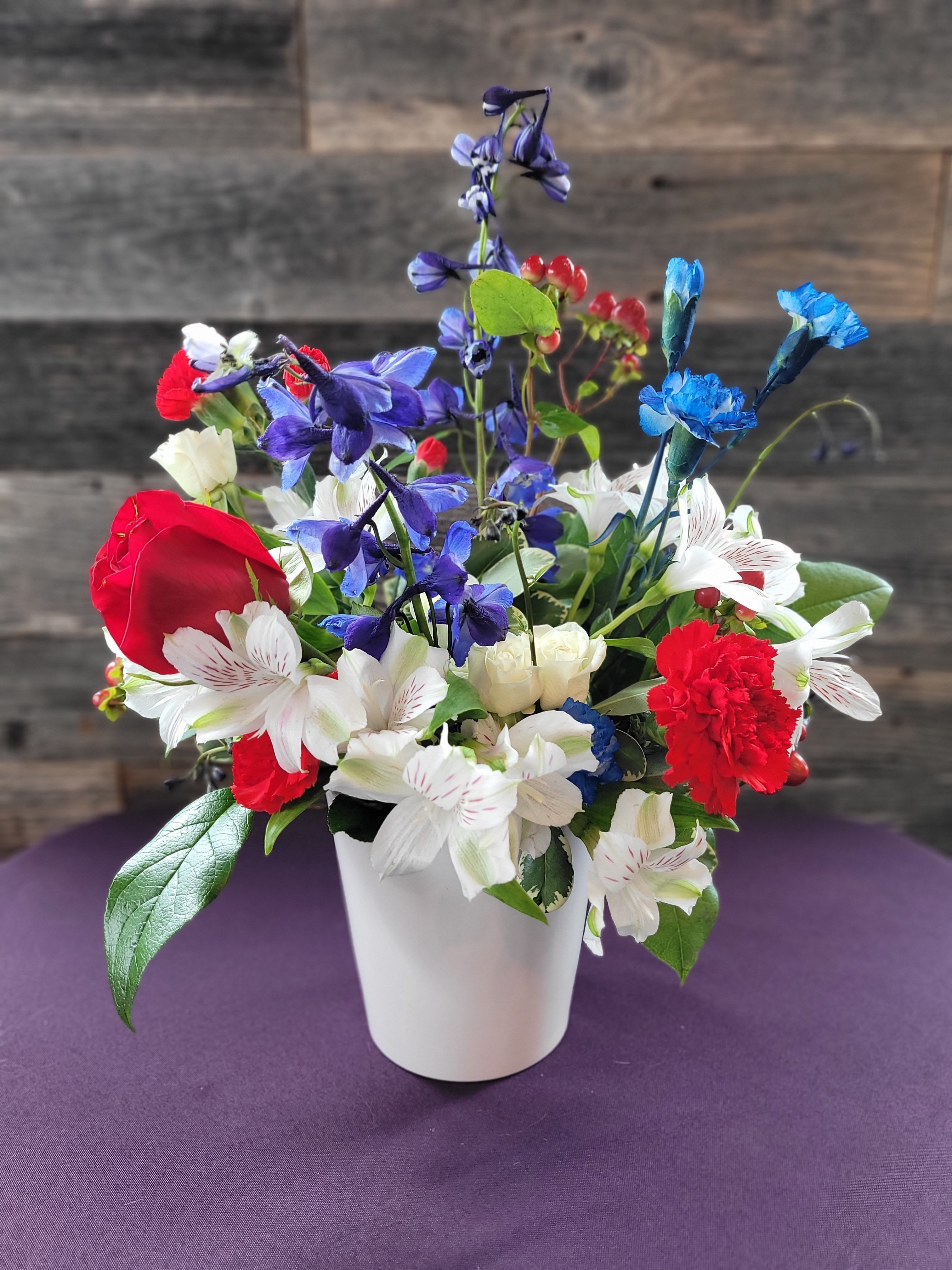 Mixed bouquet of red, white, and blue flowers in a white vase