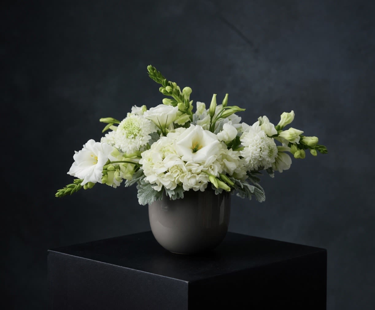 Grace and Ivory  - A timeless expression of beauty and calm,  Grace and Ivory features a soft blend of ivory and white blooms arranged in a modern ceramic vessel. Designed with movement and balance, this arrangement evokes peace, elegance, and quiet luxury—perfect for moments of sympathy, celebration, or simply sending love.  Each design is thoughtfully handcrafted using fresh, seasonal florals and finished with lush textural accents. Subtle, refined, and effortlessly graceful, Pure Grace is a beautiful choice for any space or occasion.  Designer’s Choice florals may include lisianthus, snapdragons, hydrangea, and seasonal textural elements.
