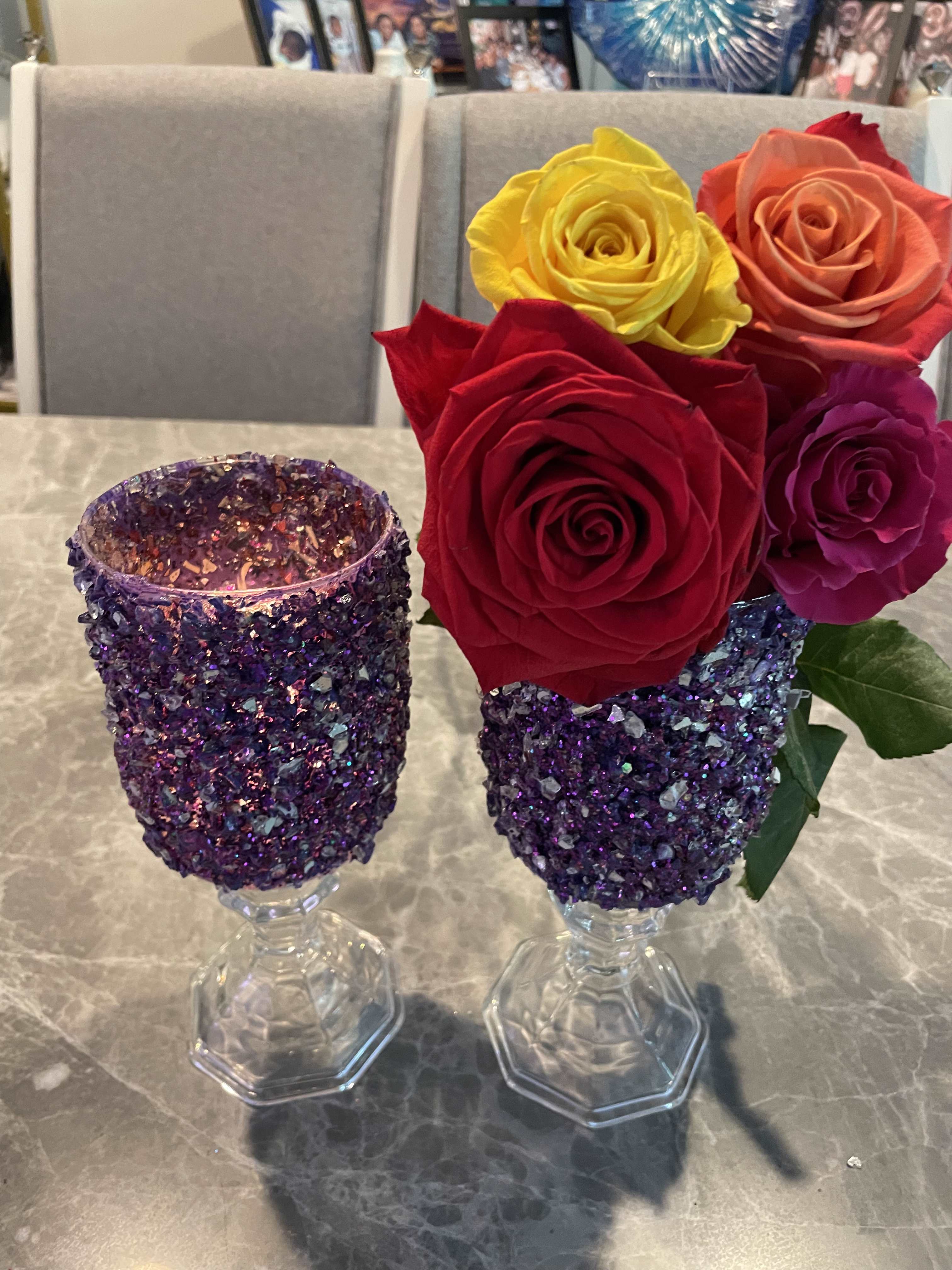 Two glitter-covered goblets hold colorful roses on a table.