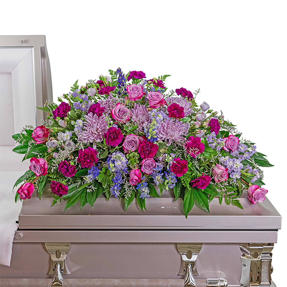 Large pink and purple floral casket spray on a light-colored casket