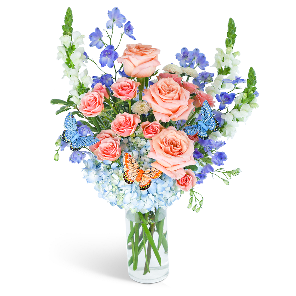 Peach roses and blue flowers in a clear glass vase with butterfly accents