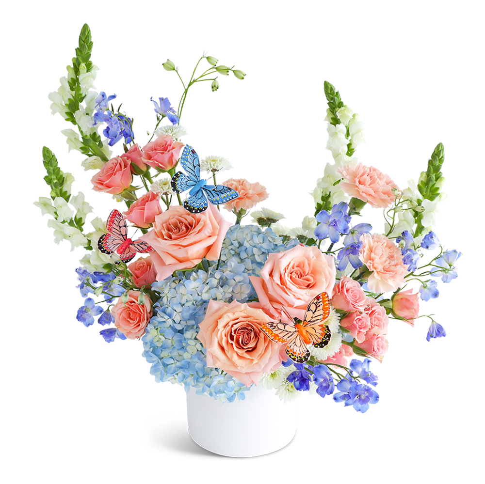 Peach roses and blue hydrangeas in a white vase with butterfly accents