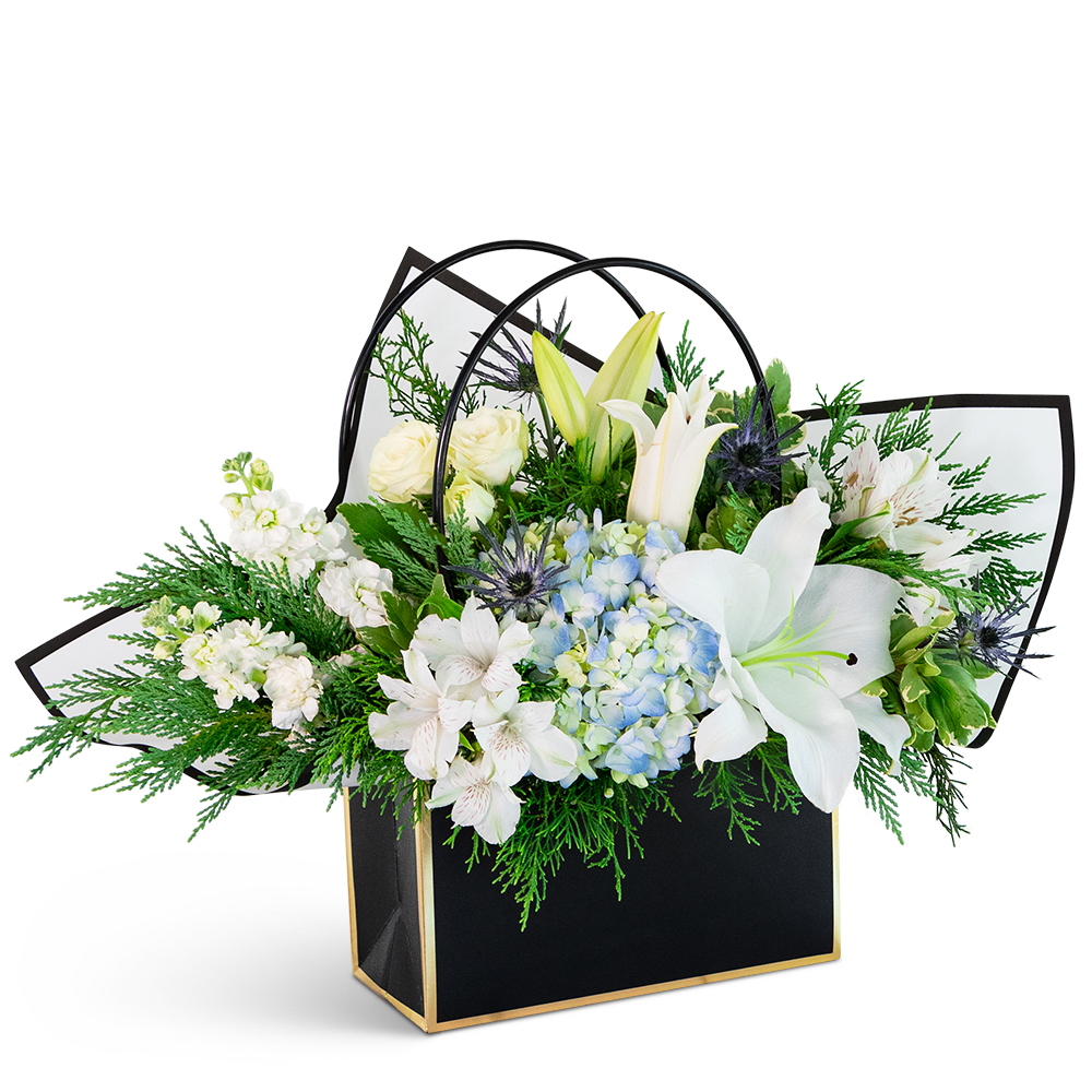 White lilies, roses, and blue hydrangea in a black gift bag