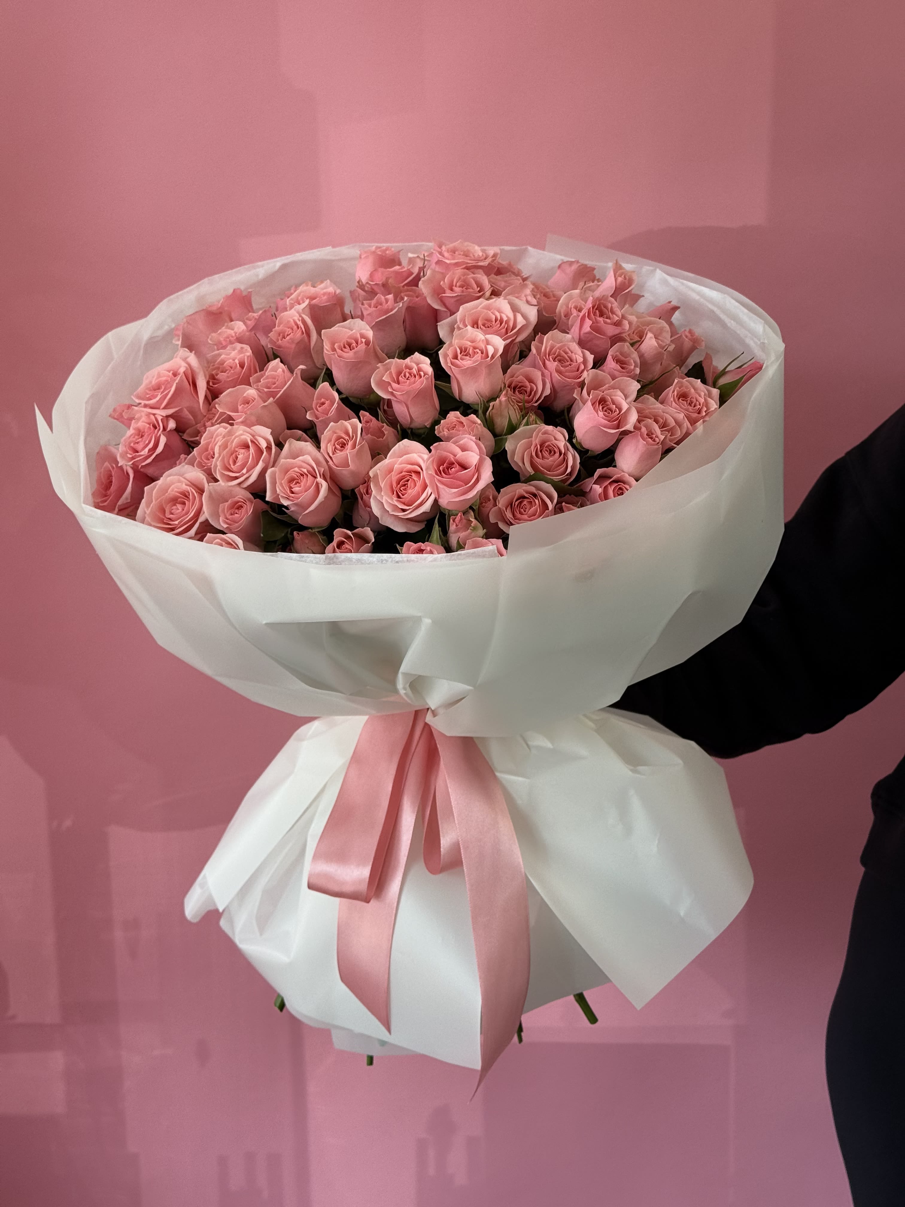 Large bouquet of pink roses wrapped in white paper with a pink ribbon