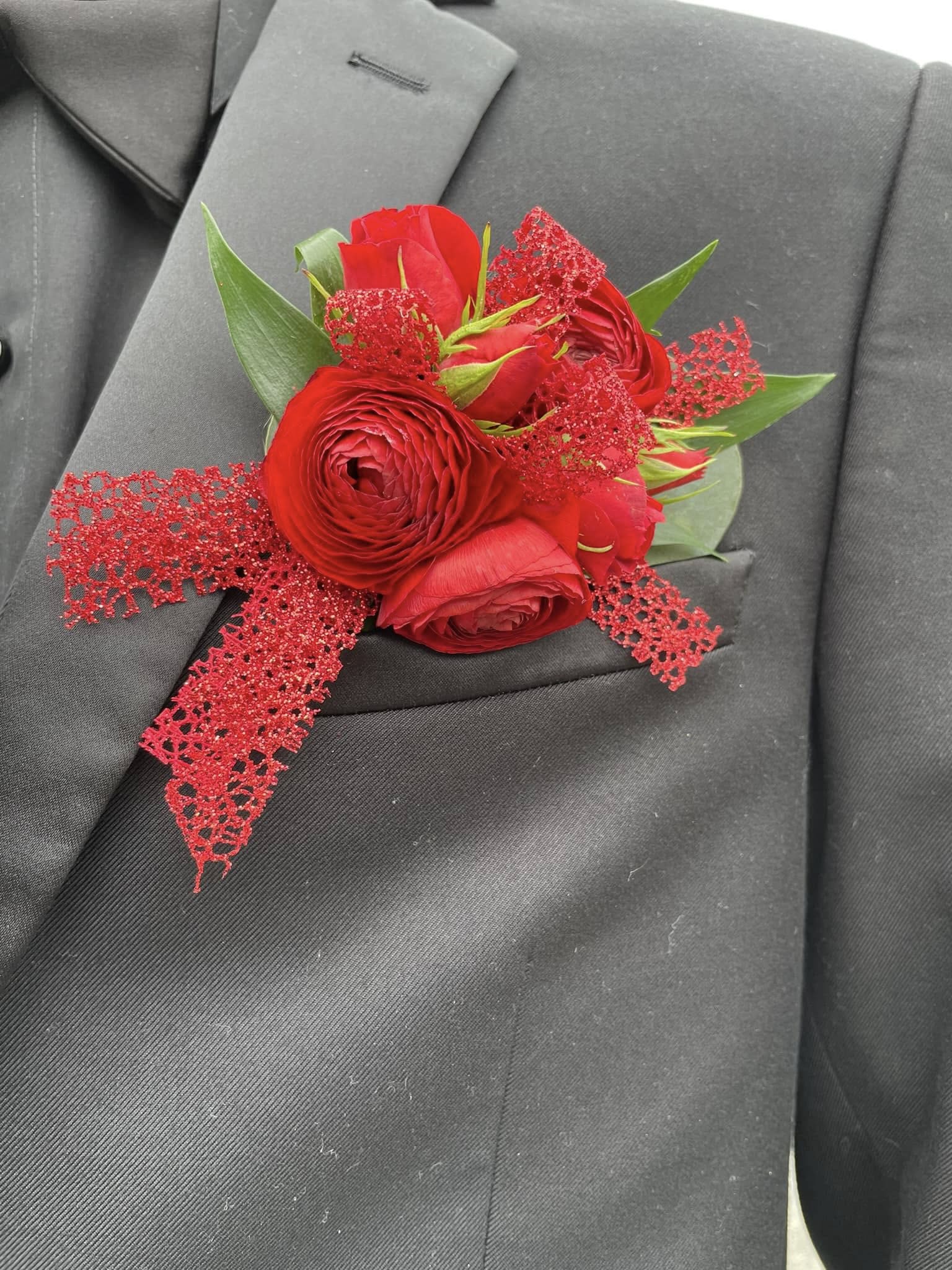 Red rose boutonniere with green leaves and glittery red ribbon on a dark suit