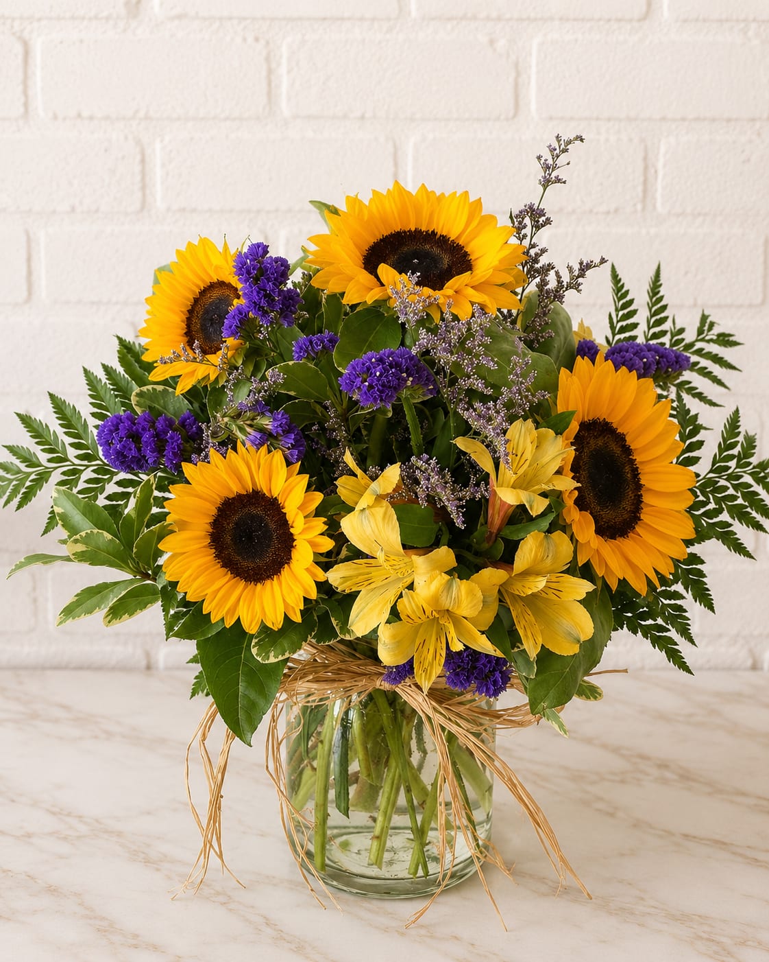 Bouquet of sunflowers and purple flowers in a glass vase with a raffia bow