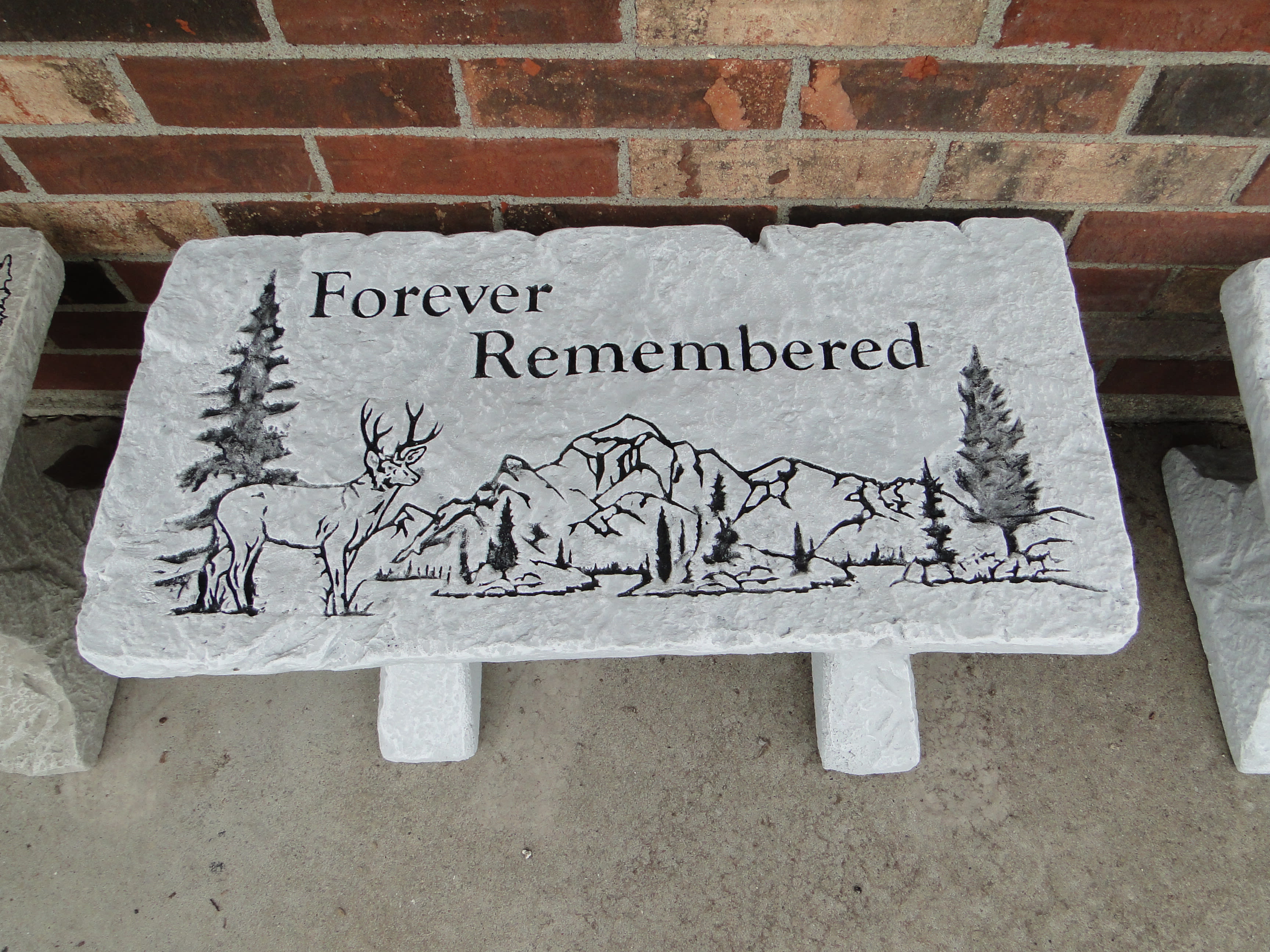 Stone memorial plaque with a deer and mountain scene and the words Forever Remembered