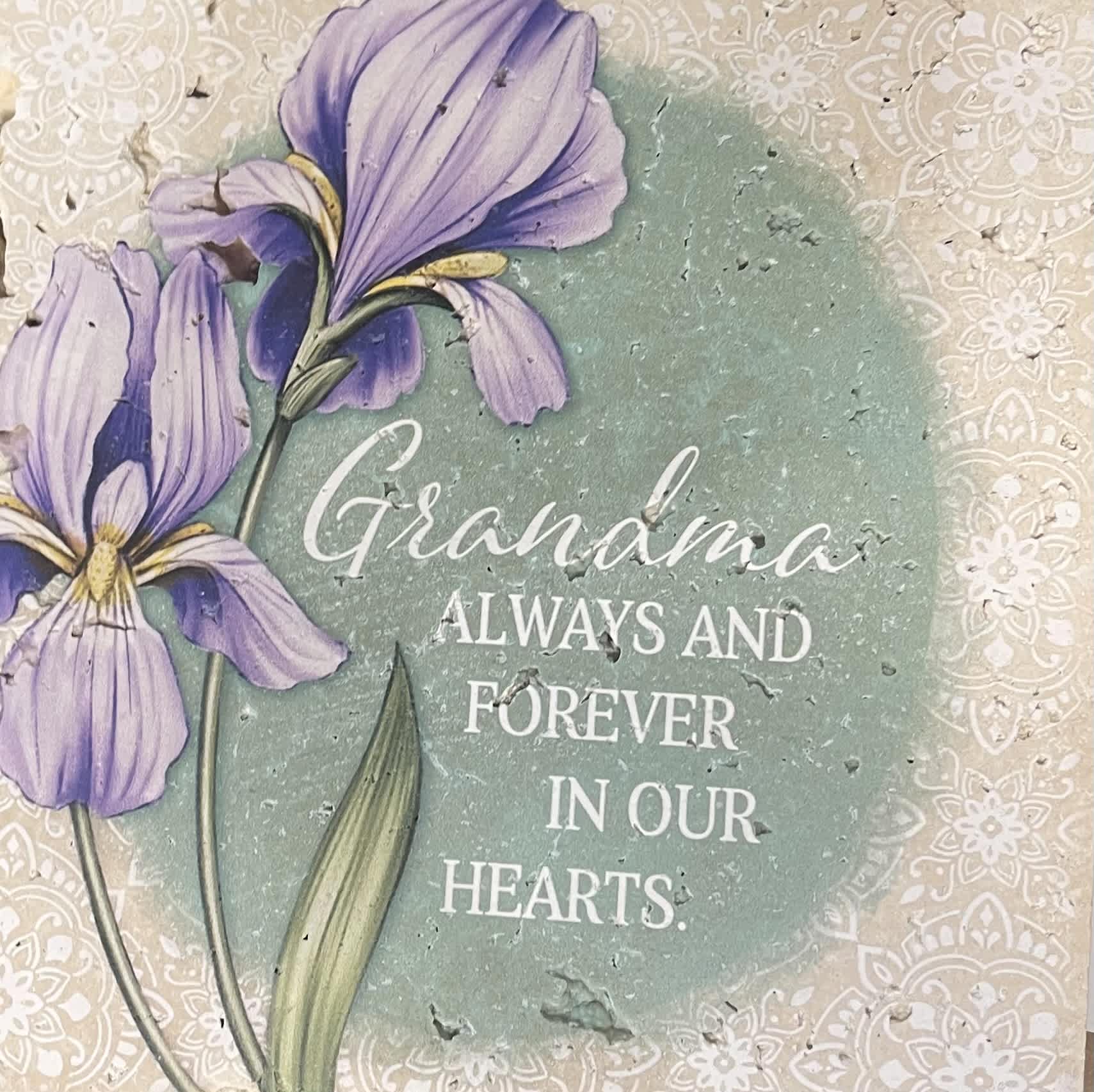 Purple flowers on a memorial plaque reading "Grandma always and forever in our hearts."