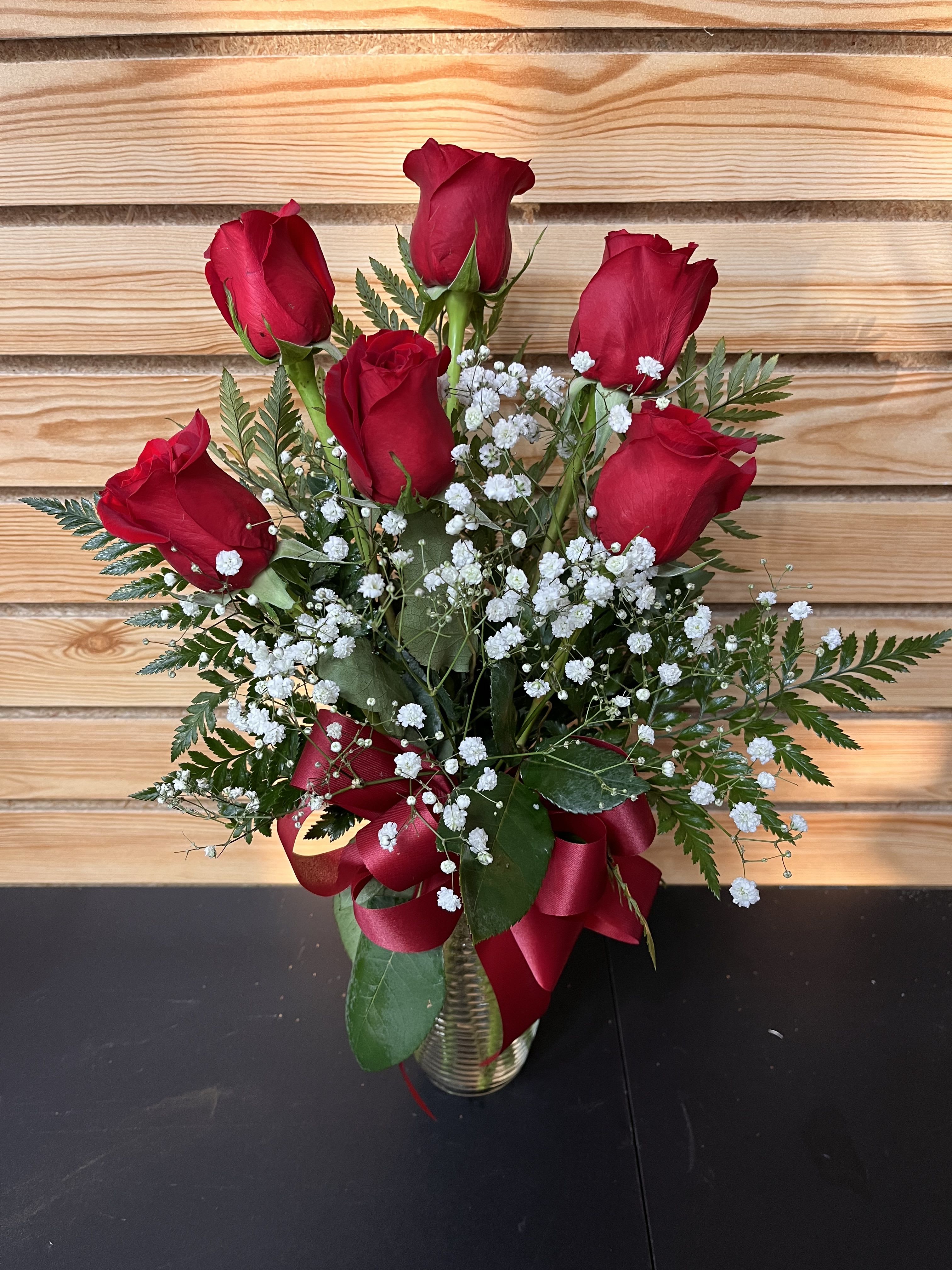 Red roses arranged in a clear vase with white baby's breath and a red ribbon