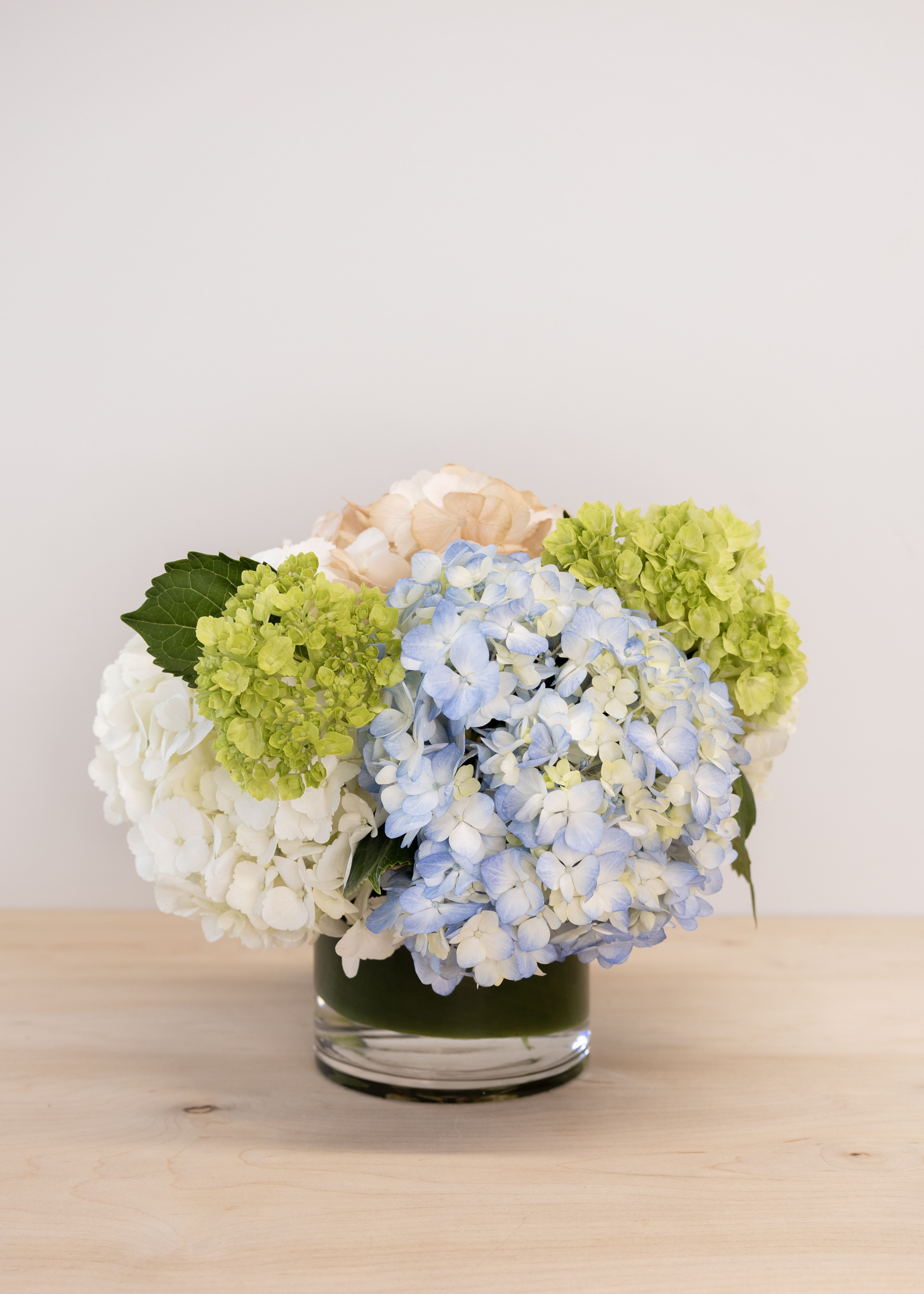 Hydrangea arrangement in a glass vase with blue, white, green, and peach blooms