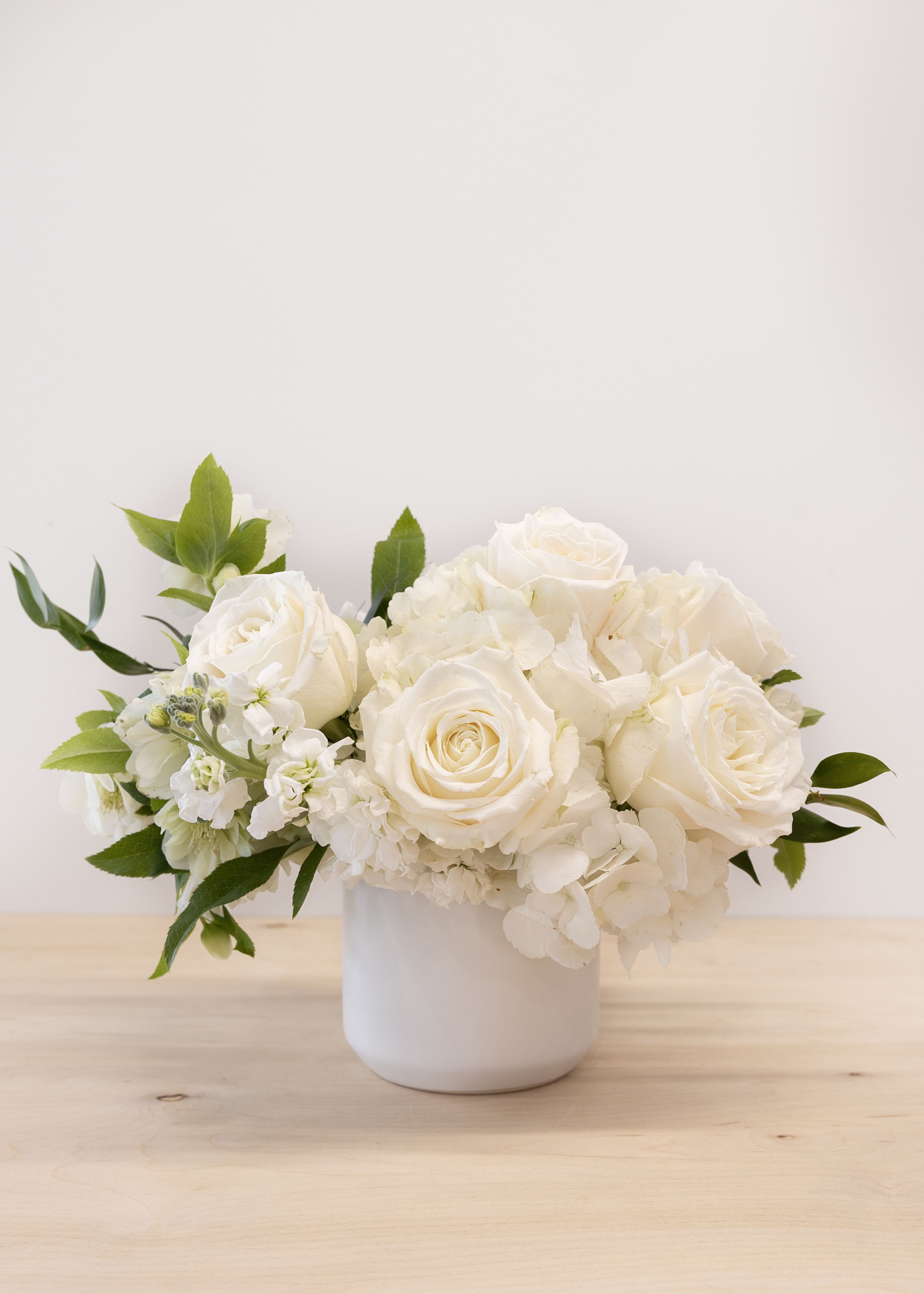 White roses and hydrangeas arranged in a white vase