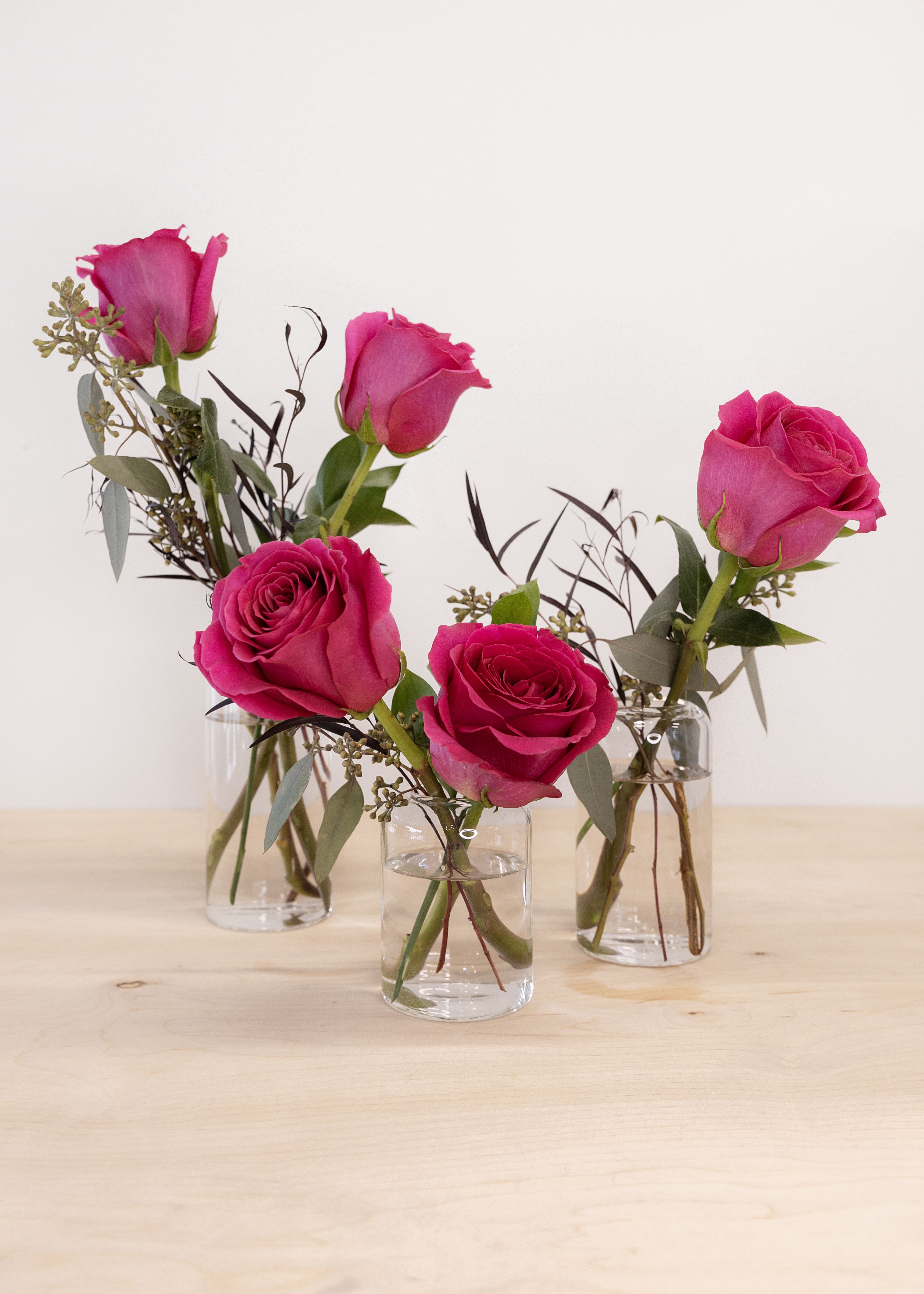 Pink roses in small clear glass vases on a wooden surface