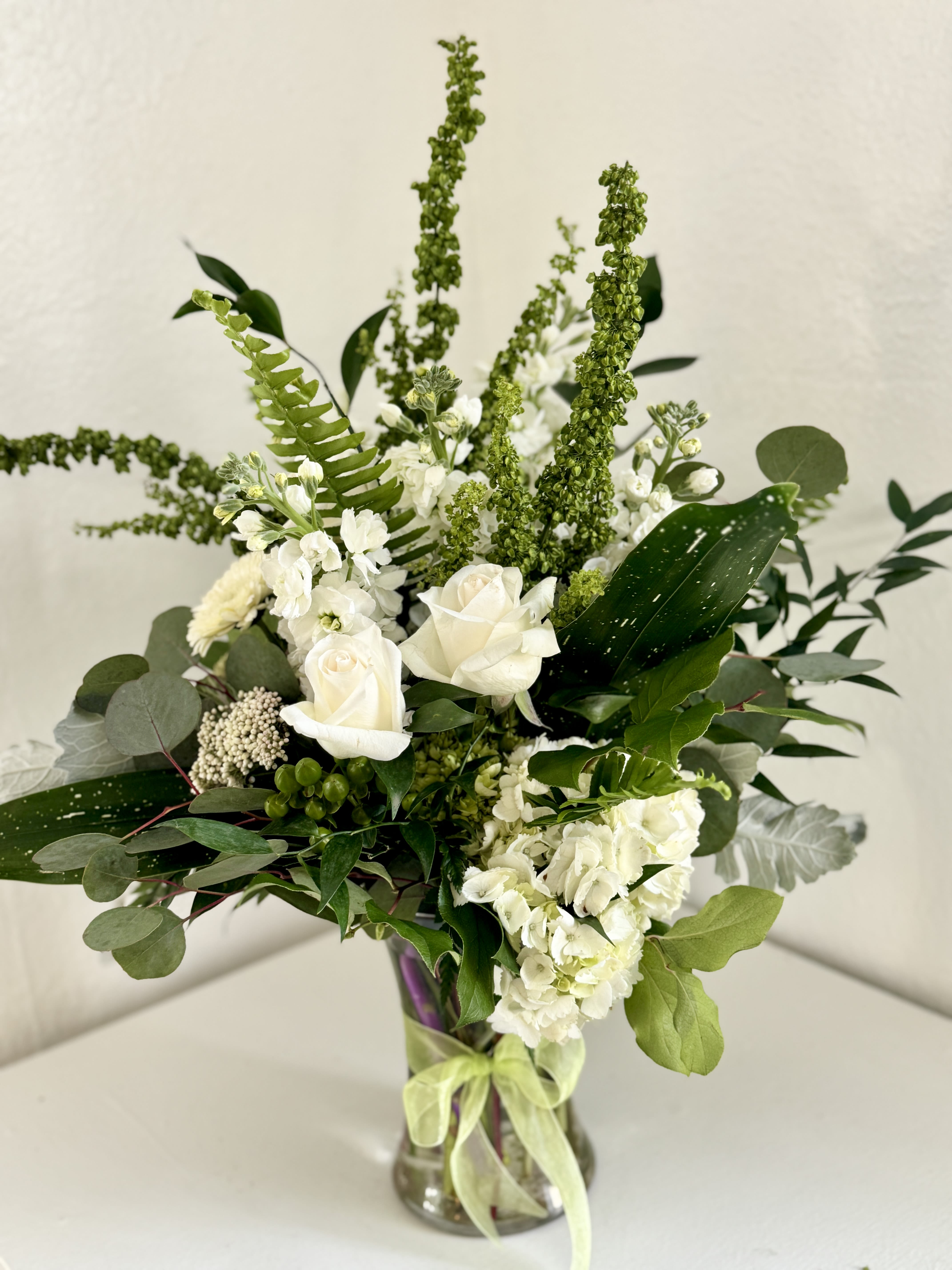 White roses and hydrangeas in a glass vase with mixed greenery