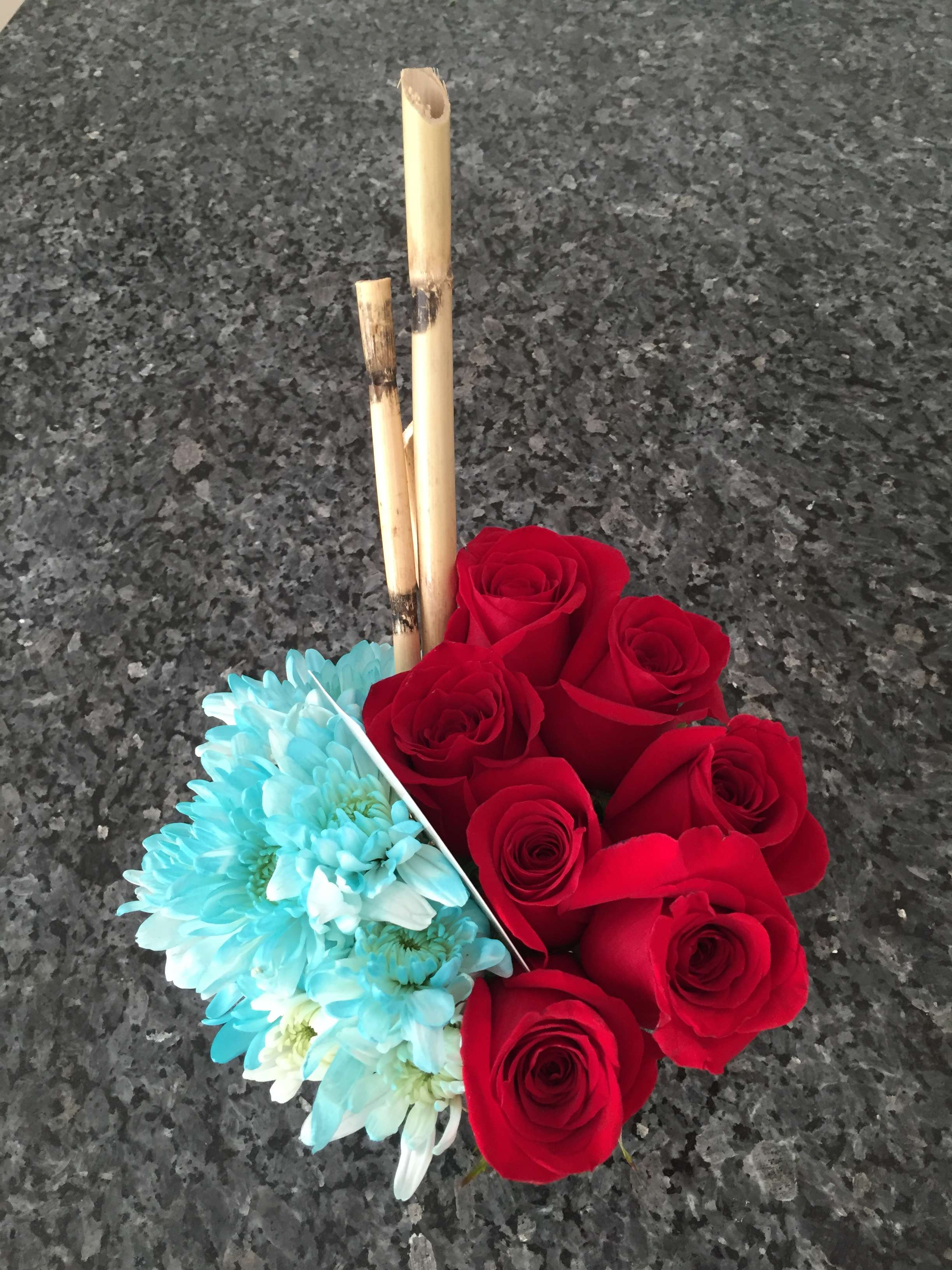 Red roses and blue daisies arranged with bamboo sticks
