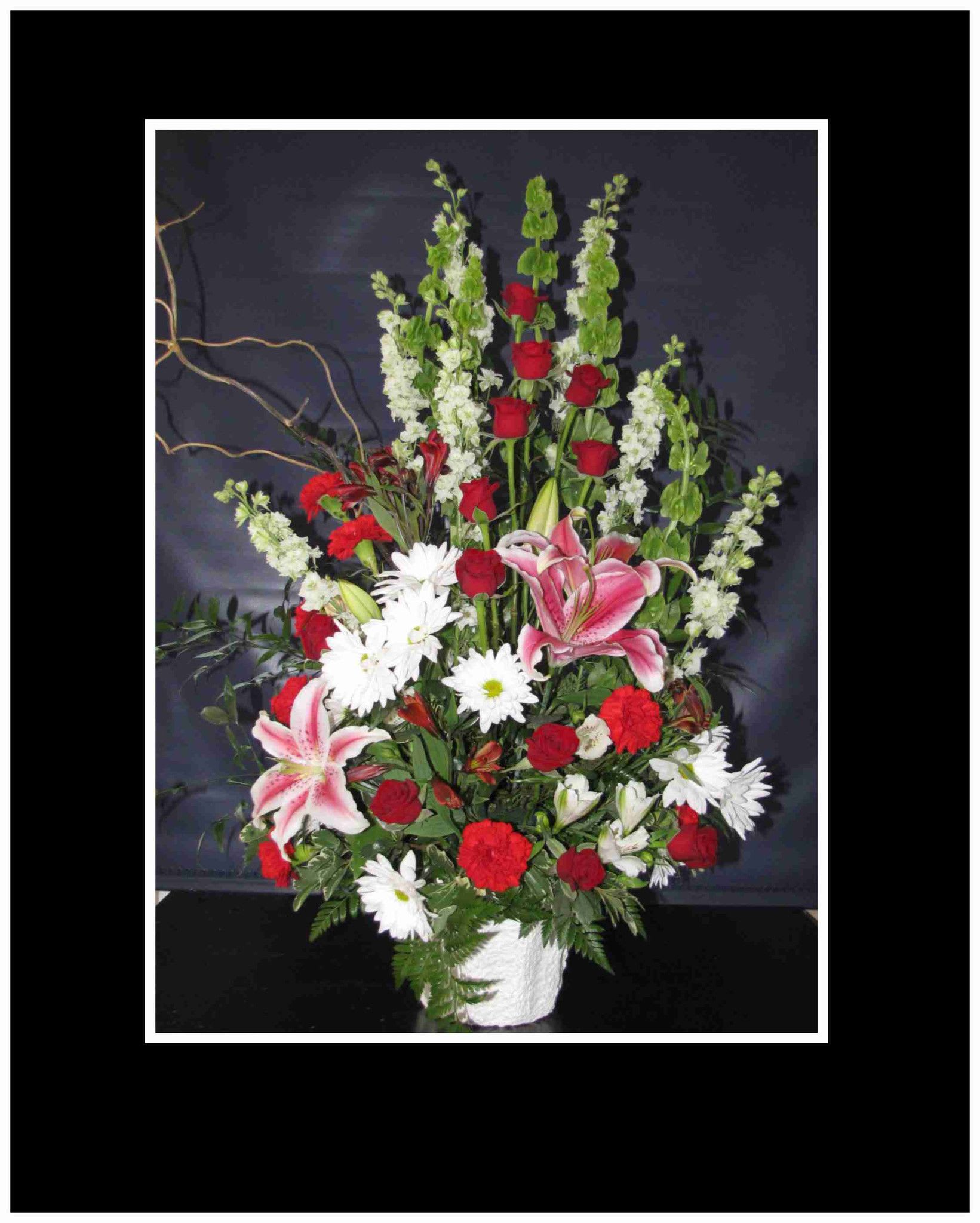 Tall mixed flower arrangement with red roses, pink lilies, and white daisies in a white vase