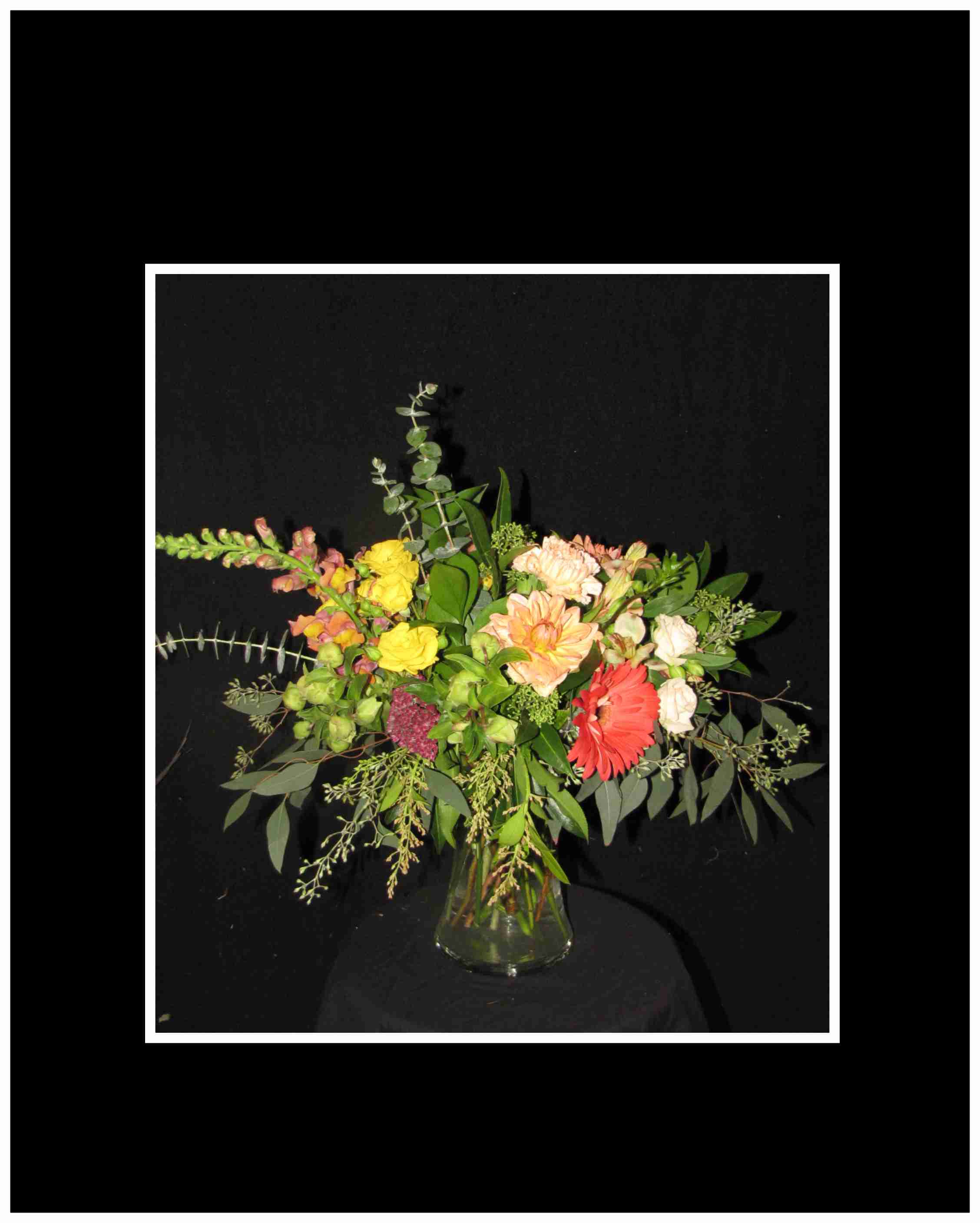 Mixed bouquet in a clear glass vase with yellow, peach, red, and white blooms