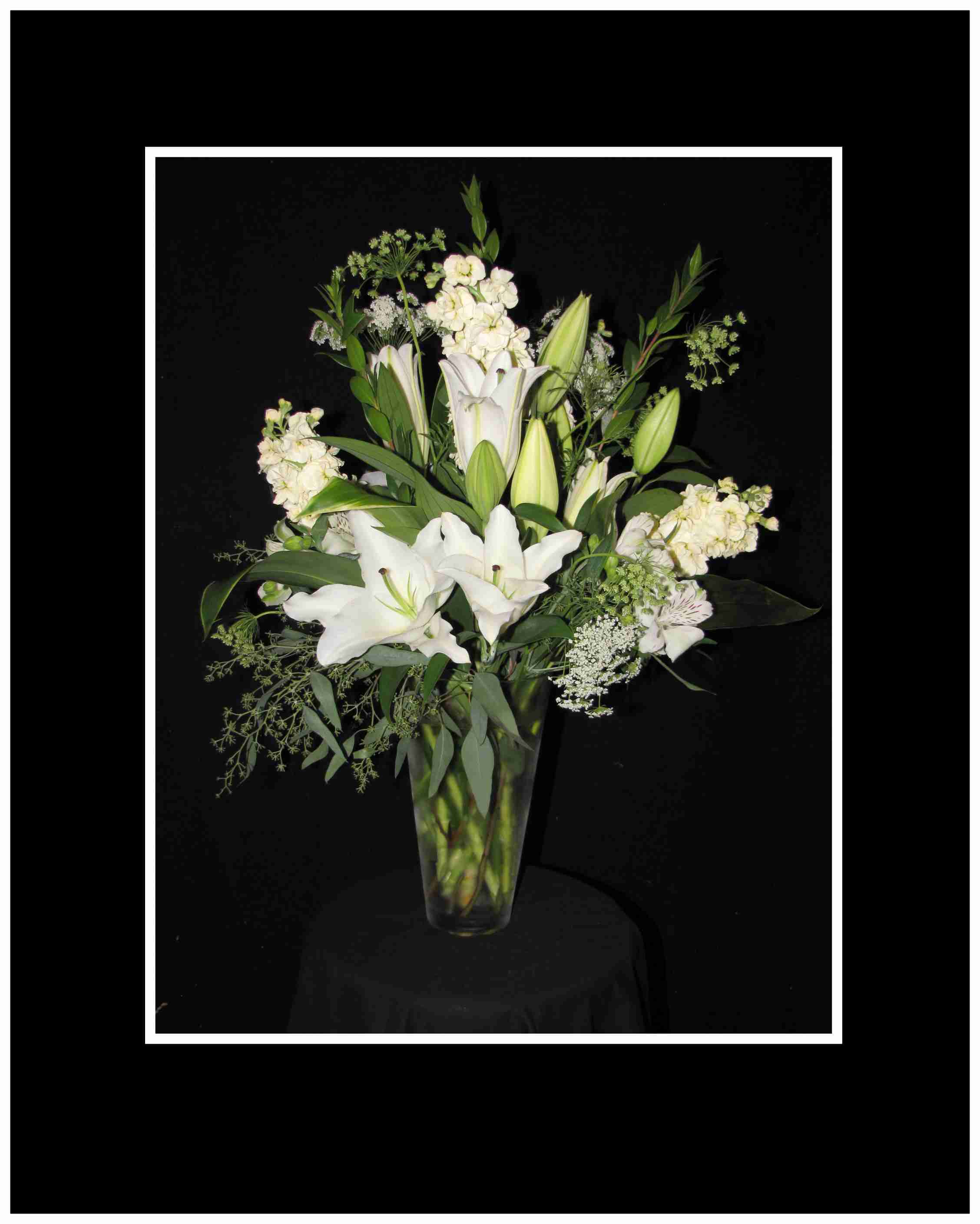 White lilies and mixed white flowers in a tall glass vase