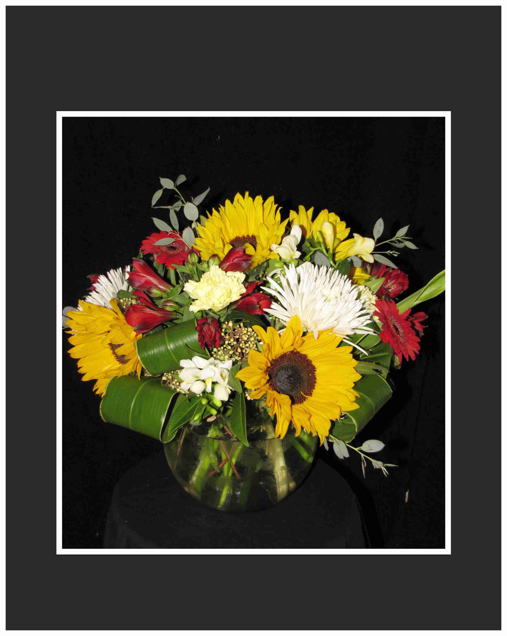 Mixed bouquet with sunflowers, red gerberas, and white blooms in a glass vase
