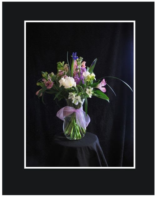 Mixed bouquet of pink, purple, and white flowers in a glass vase with a lavender bow