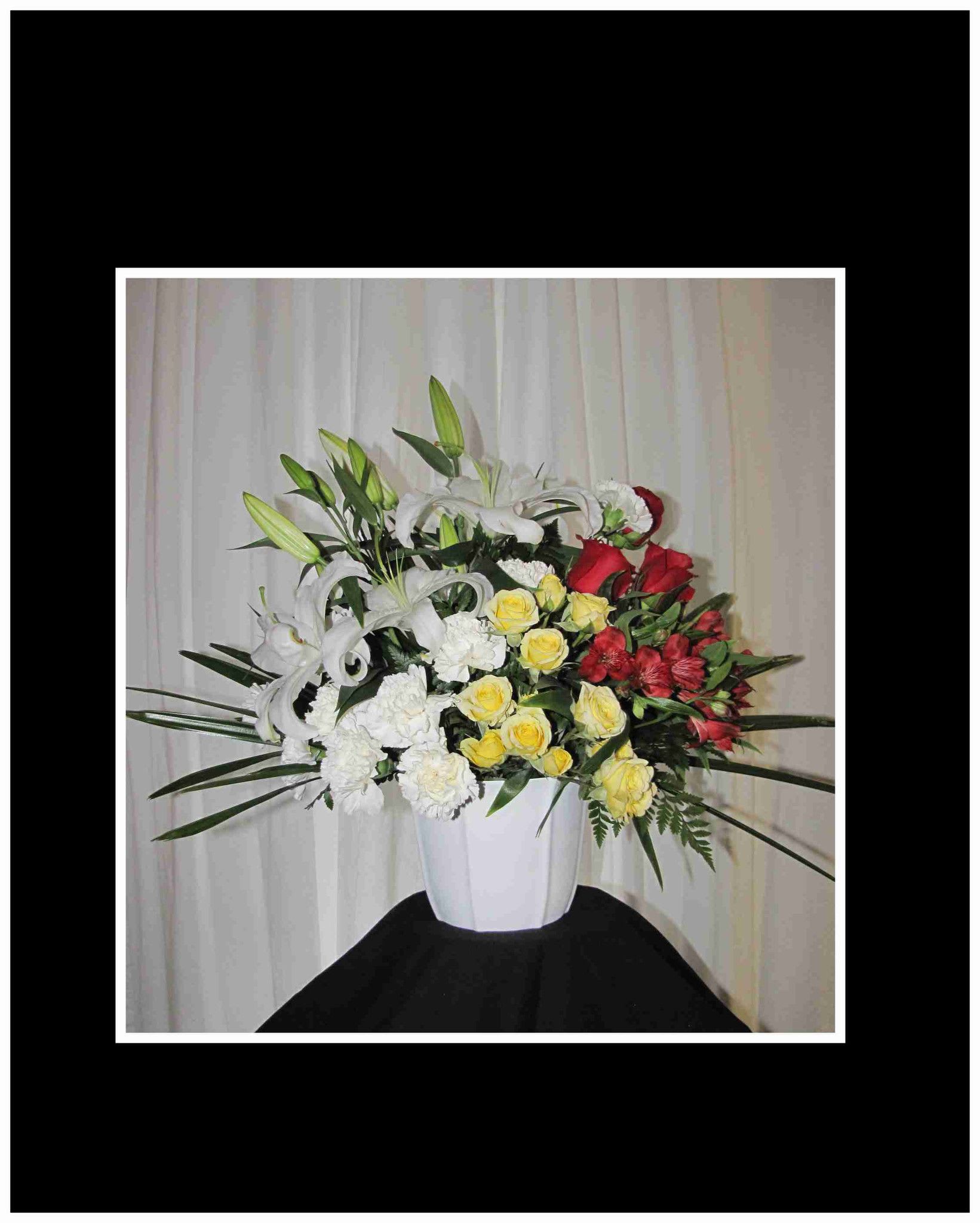 White vase arrangement with lilies, roses, carnations, and red flowers