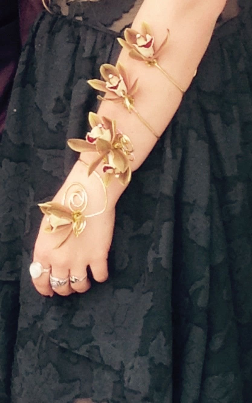 Arm wearing a gold orchid bracelet over a black dress