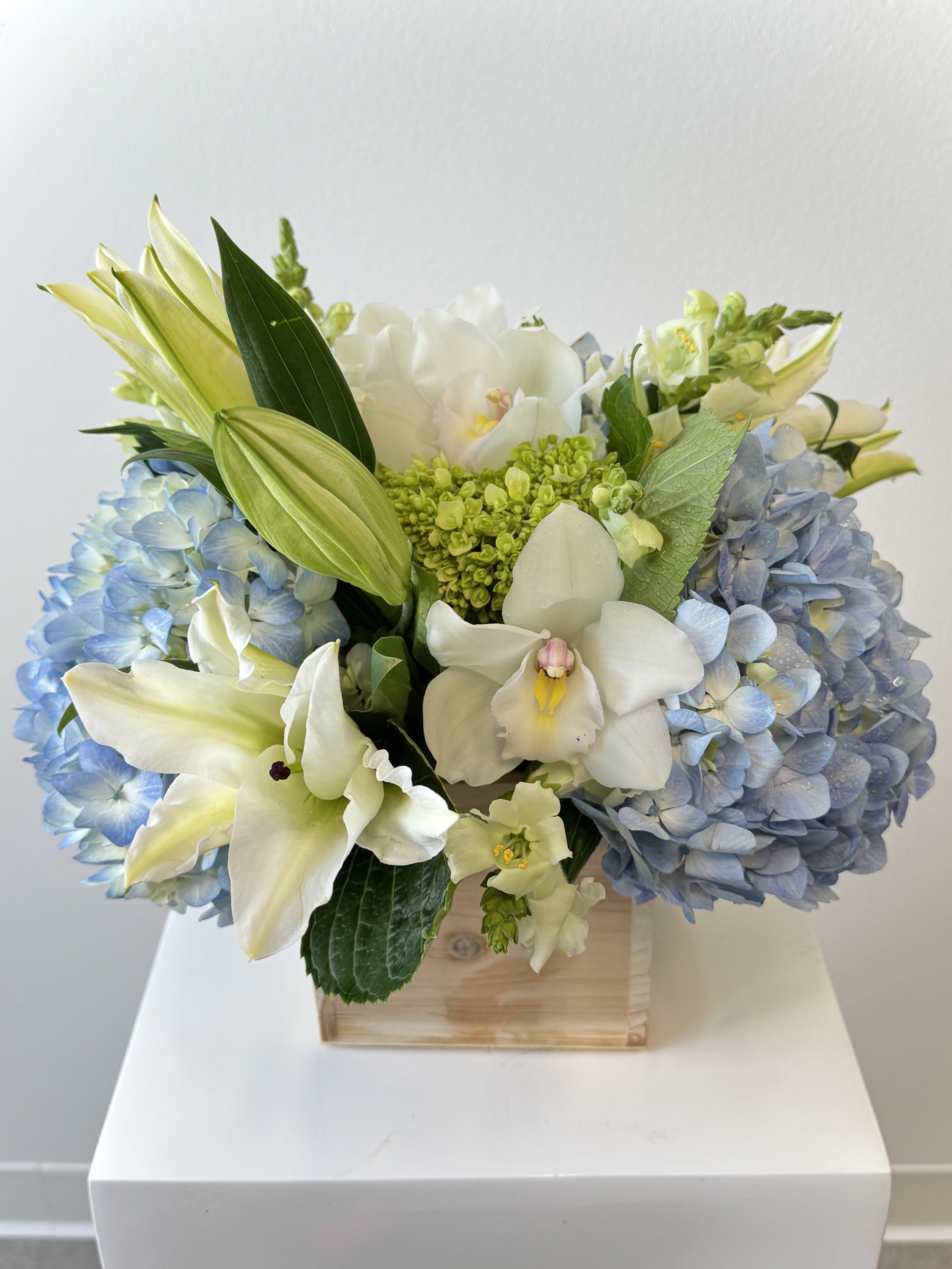Blue hydrangeas and white orchids arranged in a wooden box