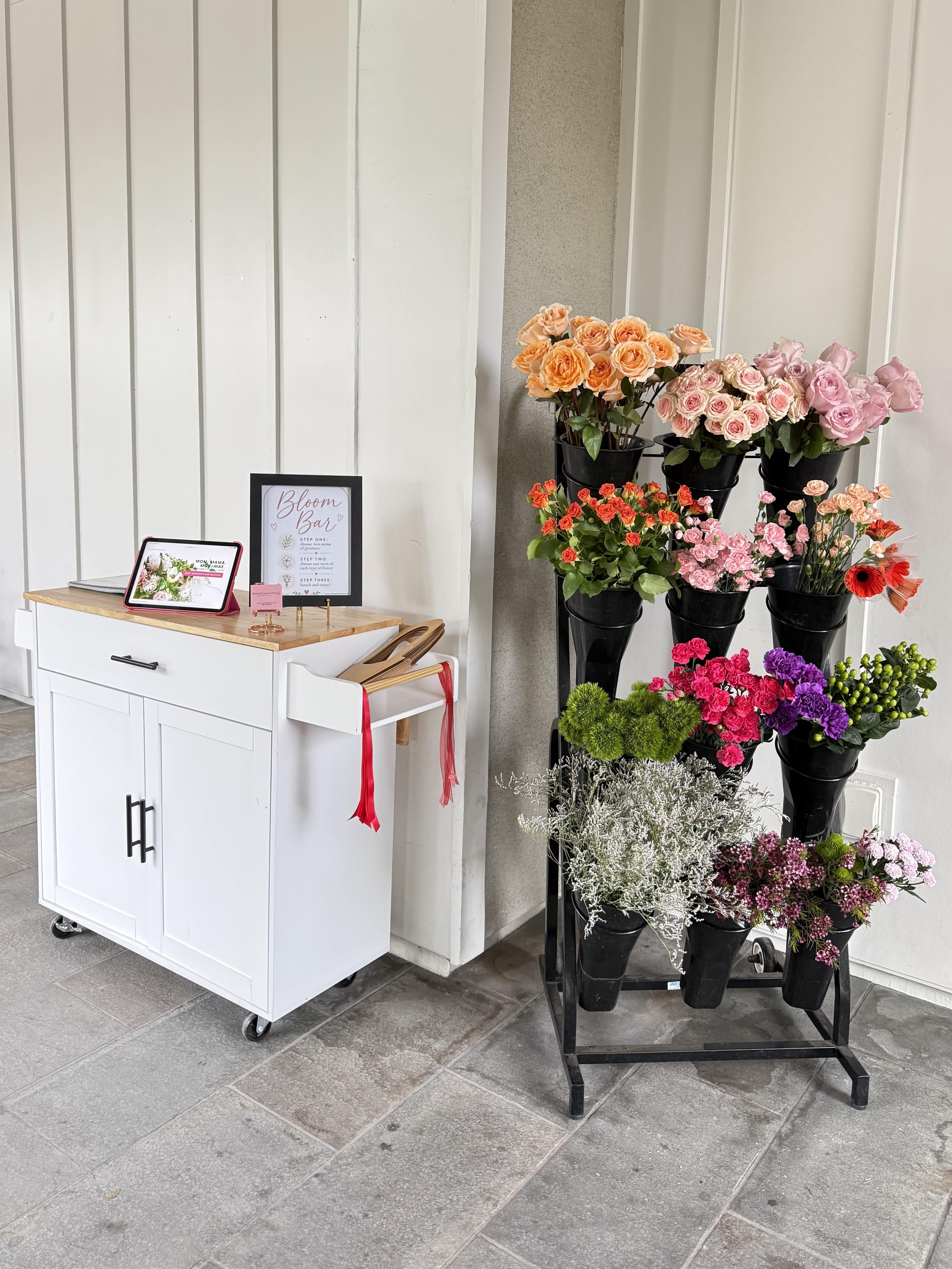 Bloom Bar - Add a fun and interactive floral element to your event with our Flower Stand Rental, designed for guests to create their own custom bouquets. Perfect for weddings, bridal showers, baby showers, corporate events, birthday parties, brand activations, and special celebrations, our flower stand becomes both a beautiful display and an unforgettable experience for your guests.  Pricing is for up to 20 guests. Additional guests may be added for $20 dollars per person.   The stand is filled with a curated selection of fresh flowers and greenery, allowing guests to mix and match their favorites to design a bouquet they can take home. It creates a stunning visual feature while giving guests a creative activity during the event.  Every flower stand rental includes a personal consultation prior to delivery to determine your preferred color palette, flower varieties, and overall floral style so the display perfectly complements your event.  Flower Stand Rental Includes: • Elegant multi-tier flower display stand • Fresh seasonal flowers and greenery • Buckets filled and ready for guest bouquet building • Pre-event consultation to customize colors and flower types • A unique interactive floral experience for your guests