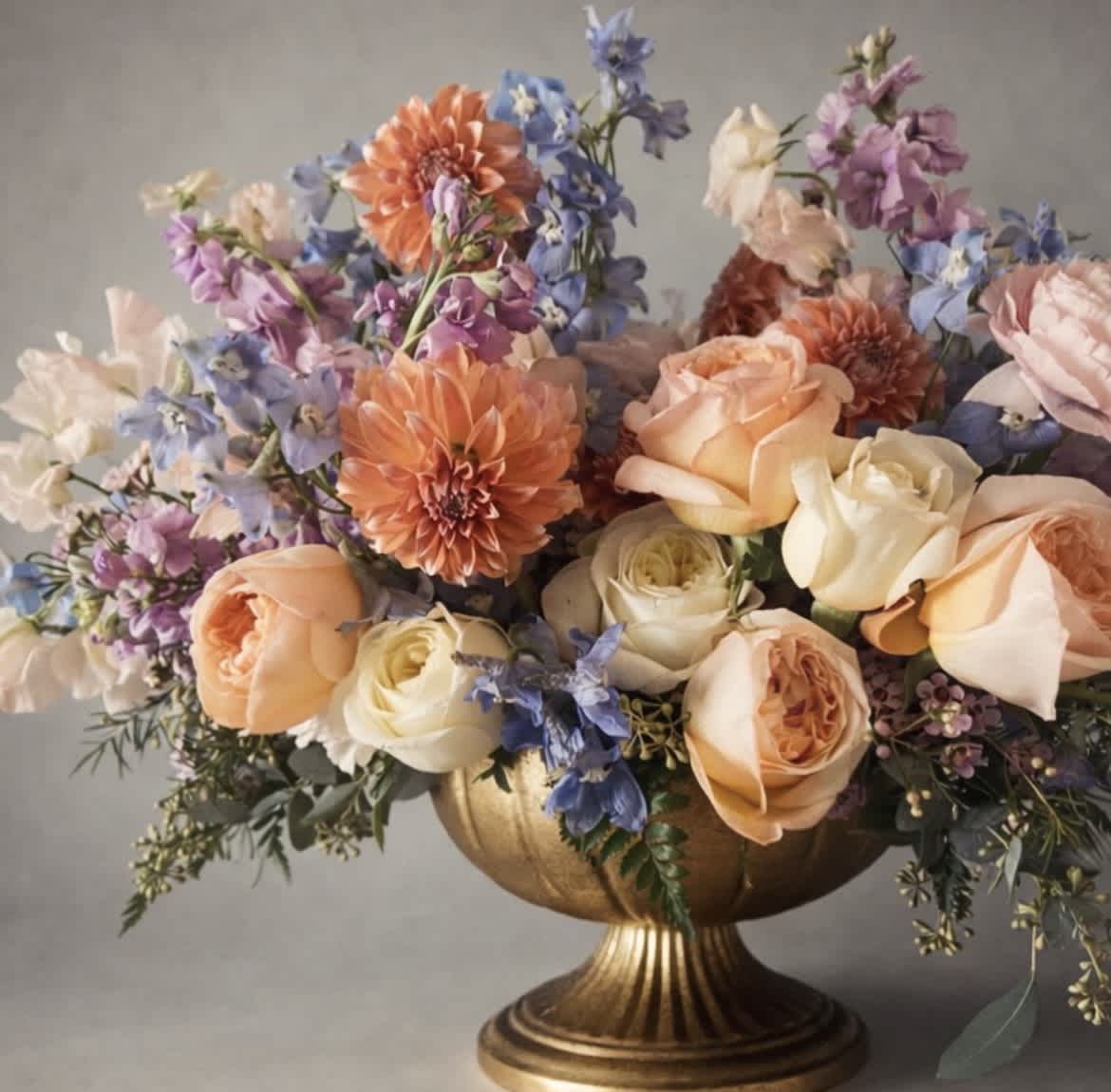 Bouquet of peach roses, orange dahlias, and blue-purple flowers in a gold vase