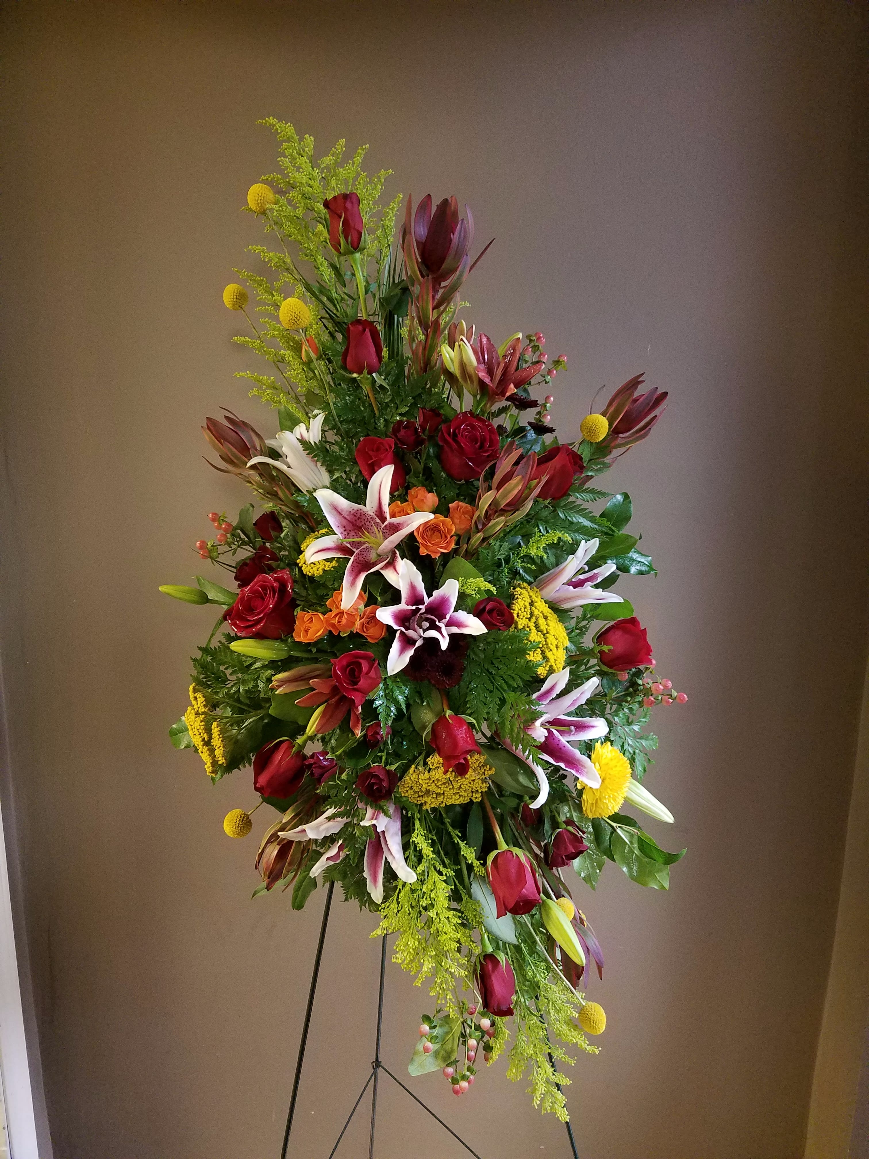 Tall standing floral spray with red roses, lilies, and yellow accents